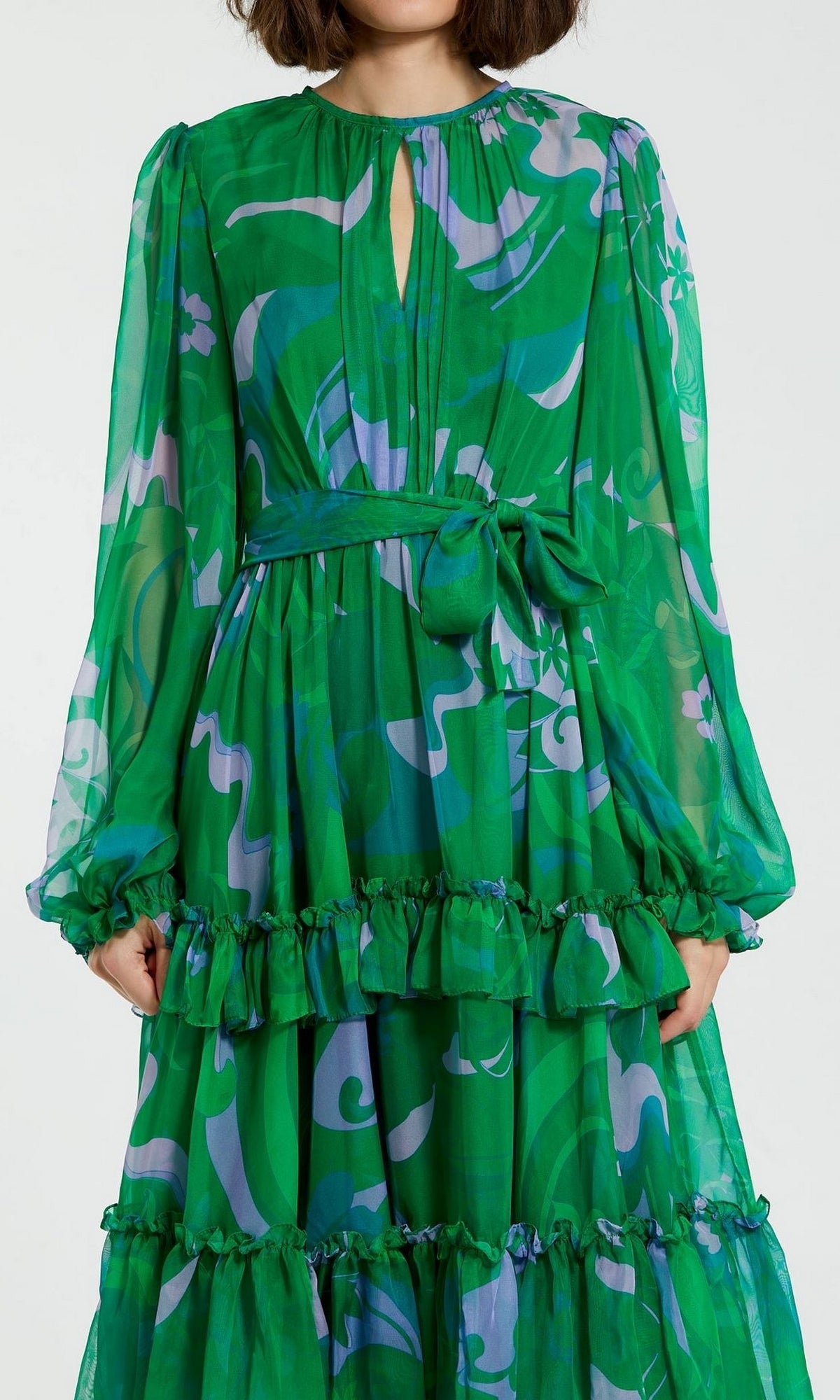 Woman wearing the Short Wedding Guest Dress 68760 by Mac Duggal, a green floral party dress with ruffle details and a tied waist belt, shown from shoulders to knees.