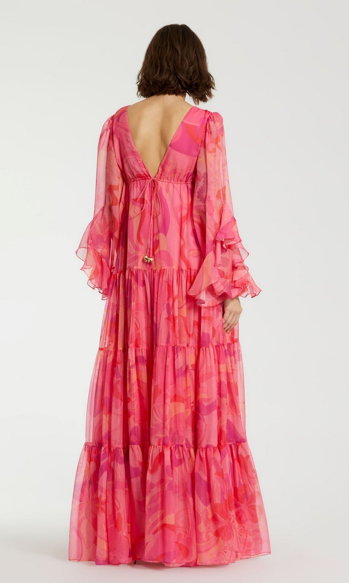 A woman wearing the Long Formal Dress 68782 by Mac Duggal—a pink floral, floor-length gown with ruffled sleeves and an open back—stands against a plain background.