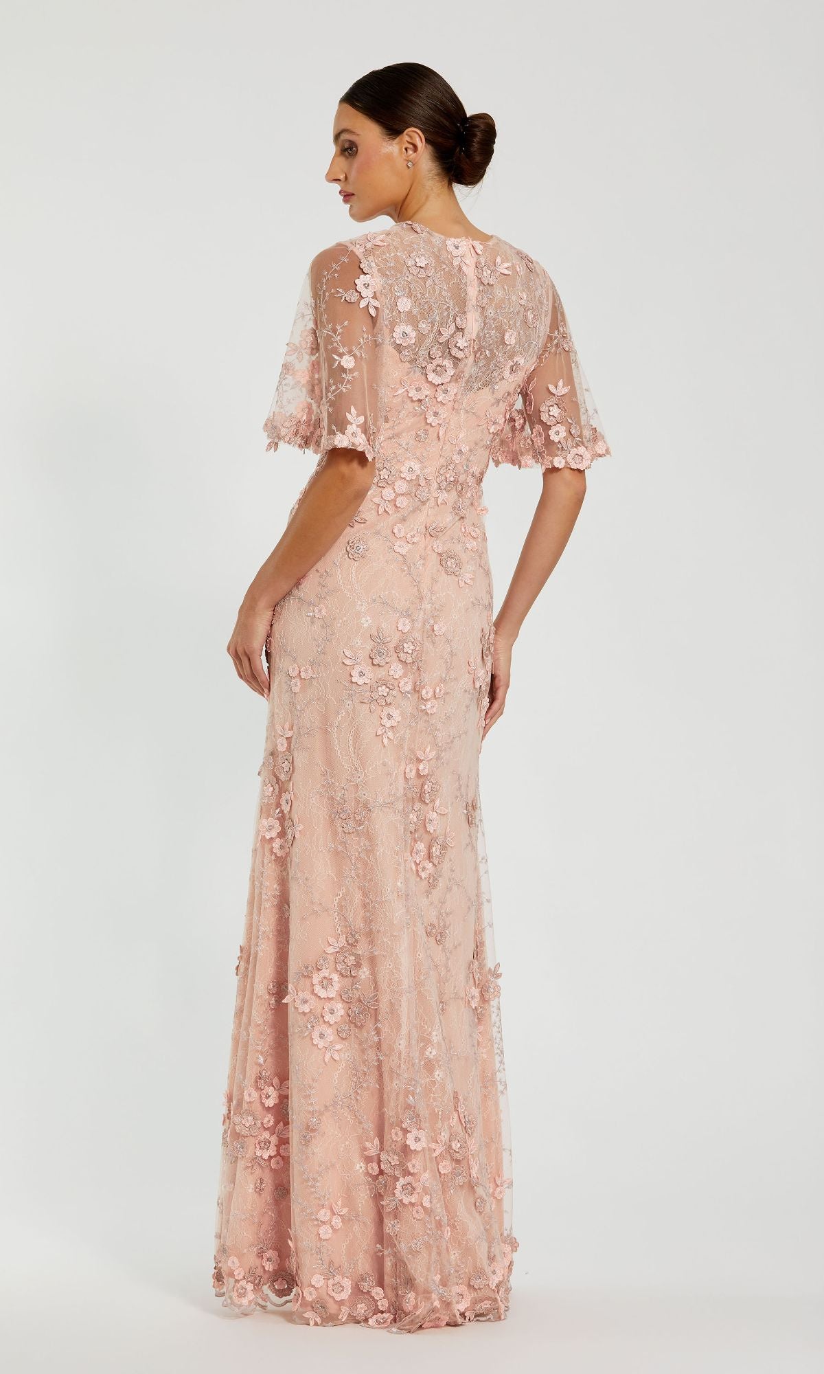 A woman stands with her back to the camera in a Flutter-Sleeve Long Formal Dress (Mac Duggal 68810), a floor-length, light pink gown featuring lace, floral embroidery, and short sleeves against a plain background.