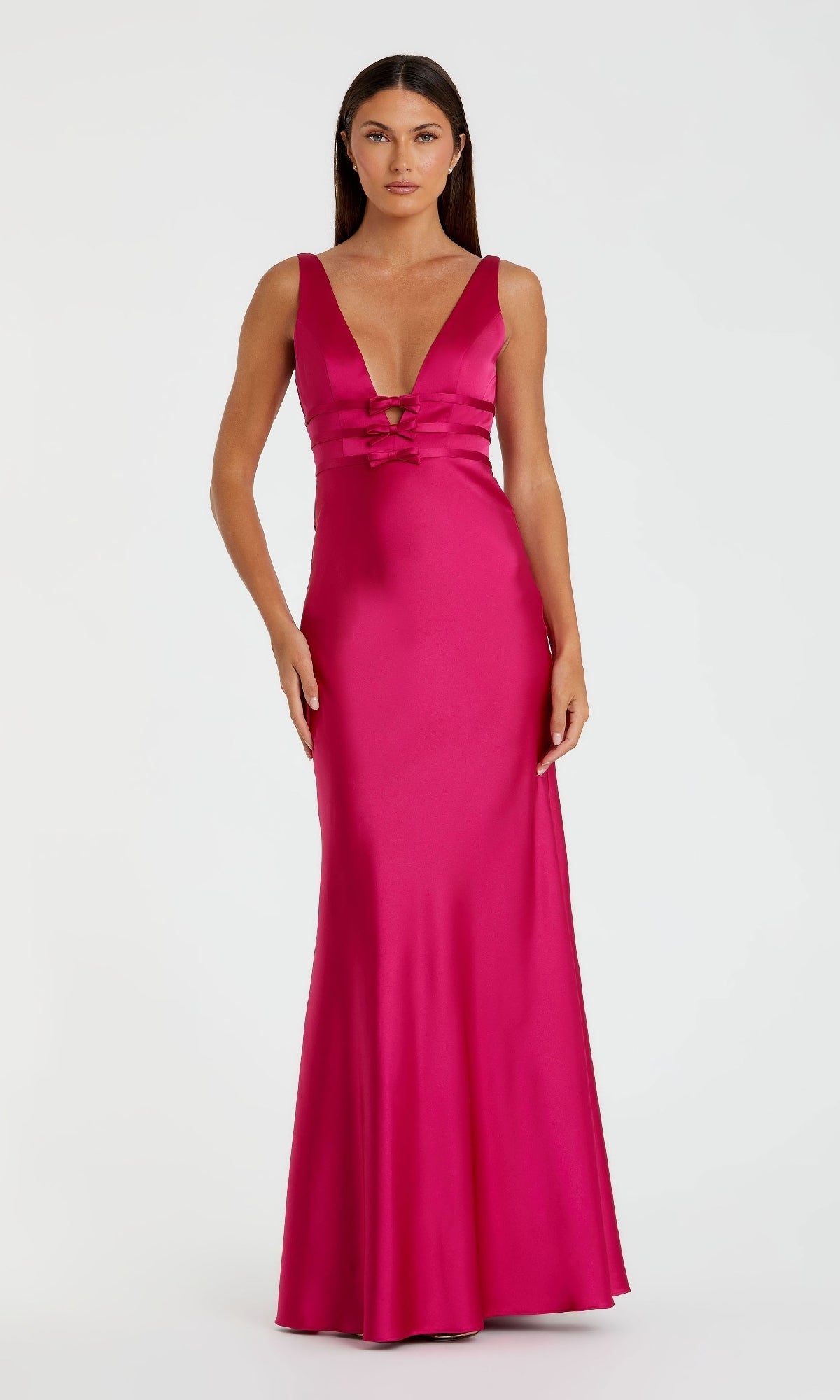 A woman stands against a white background wearing the Mac Duggal 68855 Raspberry Long Satin Prom Dress, featuring strappy back, floor-length silhouette, deep V-neckline, and lace-up front detail.