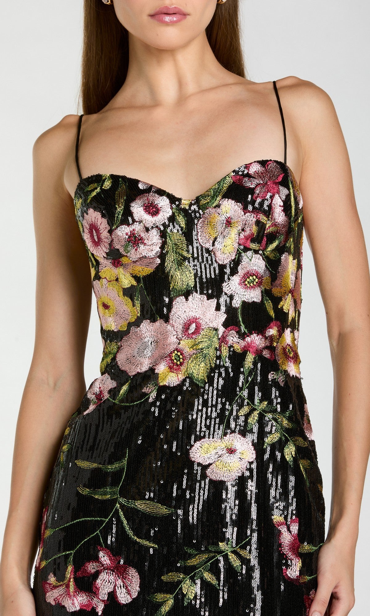 A woman wears the Long Formal Dress: Mac Duggal 68896—an elegant black gown with thin straps, featuring pink, yellow, and green floral embroidery and shimmering sequins.