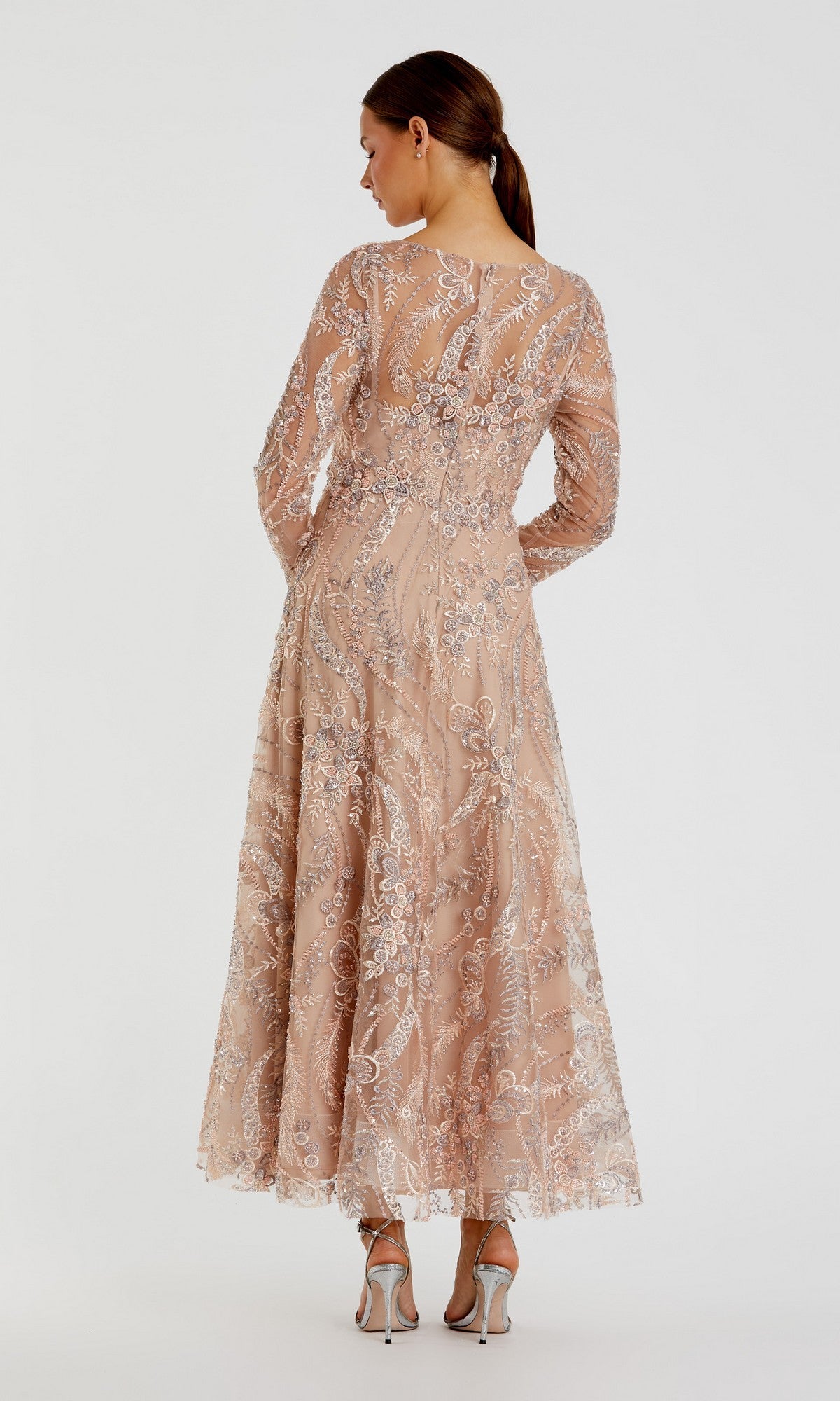 A woman wearing the Mac Duggal 68906 ankle-length party dress with long sleeves, nude-colored lace accented by silver embellishments, and a graceful a-line skirt stands with her back to the camera, paired with silver high-heeled sandals.