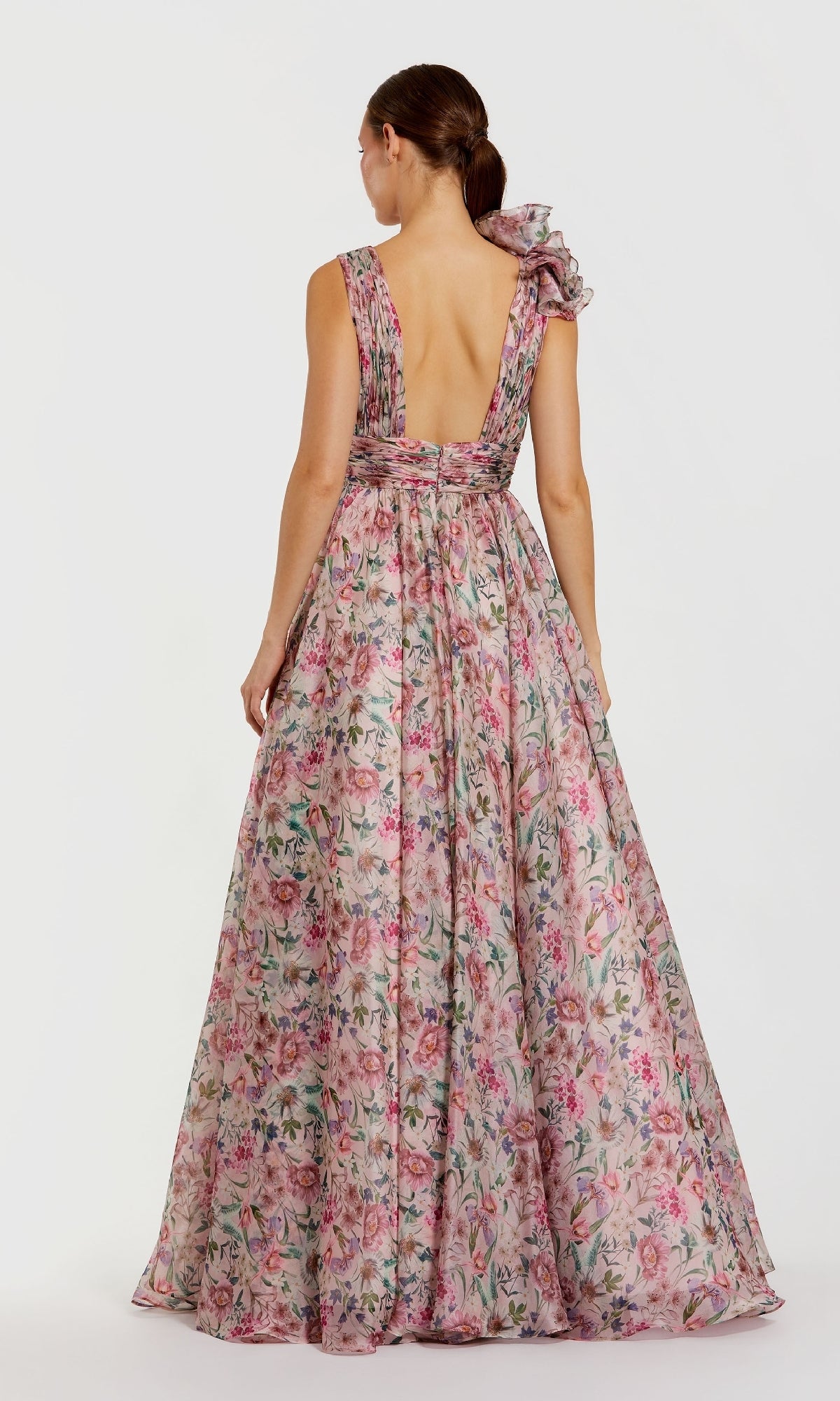 A woman faces away in the Mac Duggal 68947 floral-print long formal dress, featuring chiffon fabric, a deep V-back, and a shoulder bow—an elegant choice for prom.