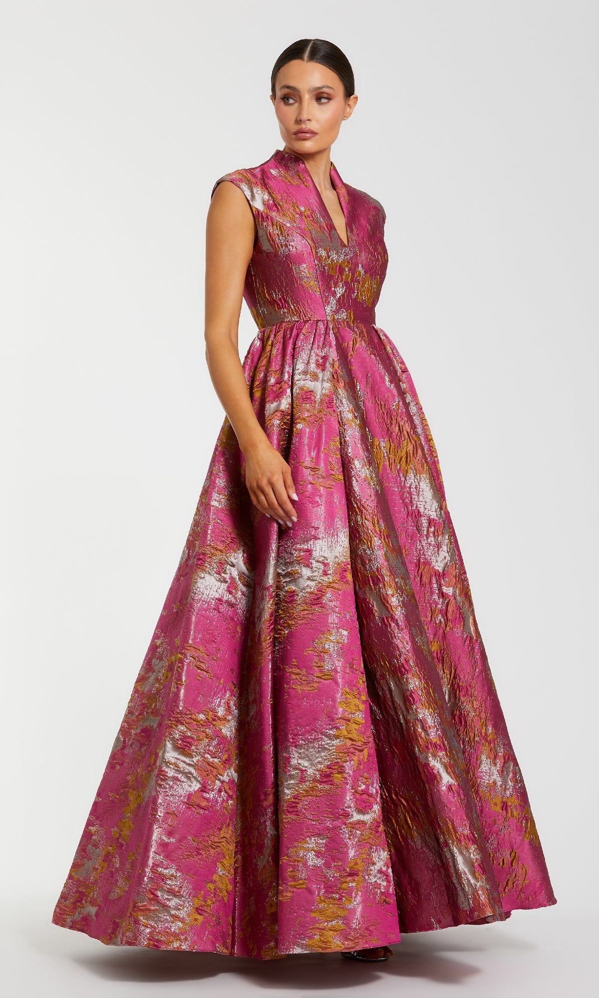 A woman wears the Long Formal Dress: Mac Duggal 68956, a floor-length, sleeveless gown featuring a metallic gold and silver textured pattern with an elegant A-line skirt, standing against a plain white background.