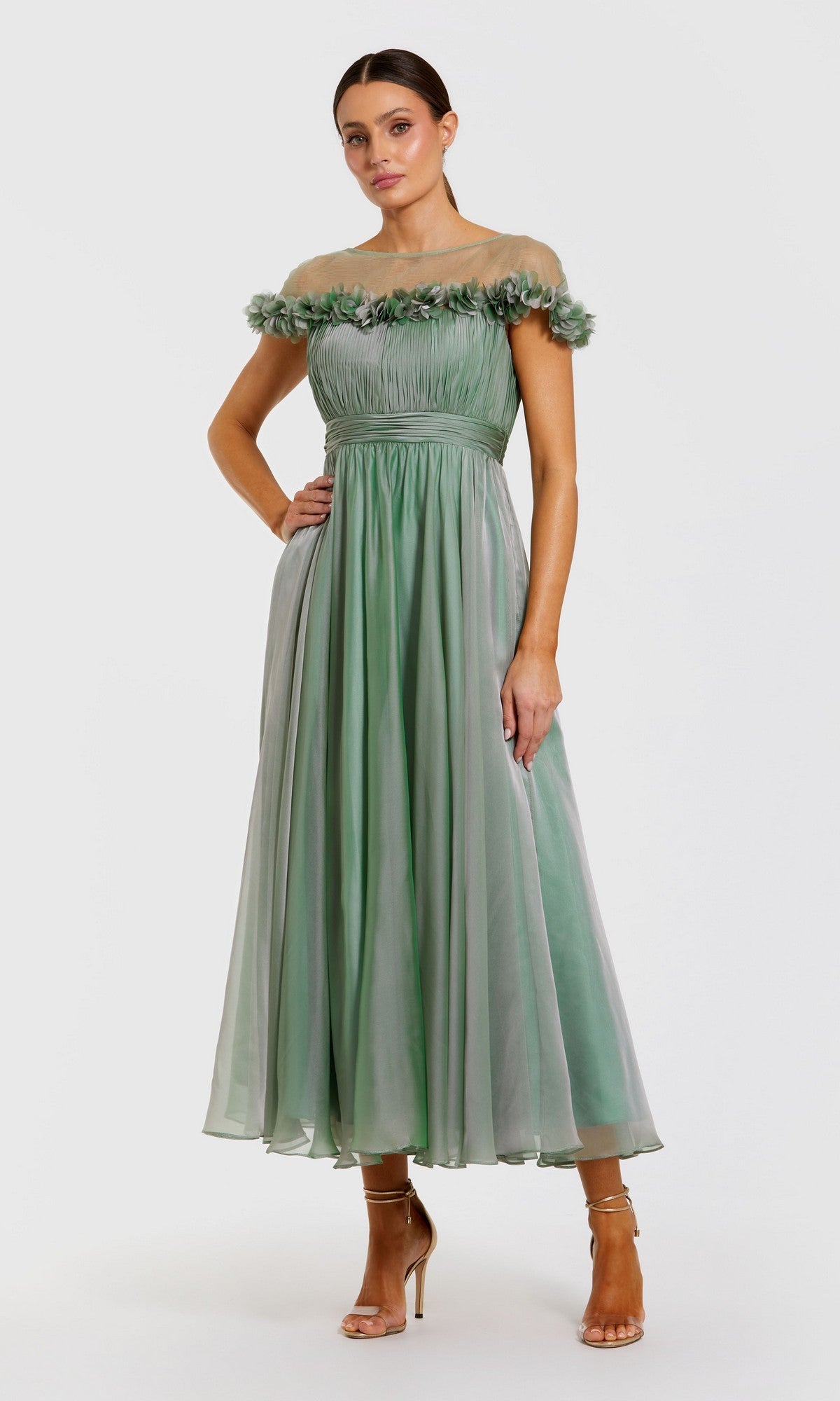 A woman wears the Mac Duggal 68966 Tea-Length Party Dress in sage, featuring an off-the-shoulder neckline with delicate floral detailing. The elegant chiffon design stands out against a plain white background, effortlessly combining sophistication and charm.