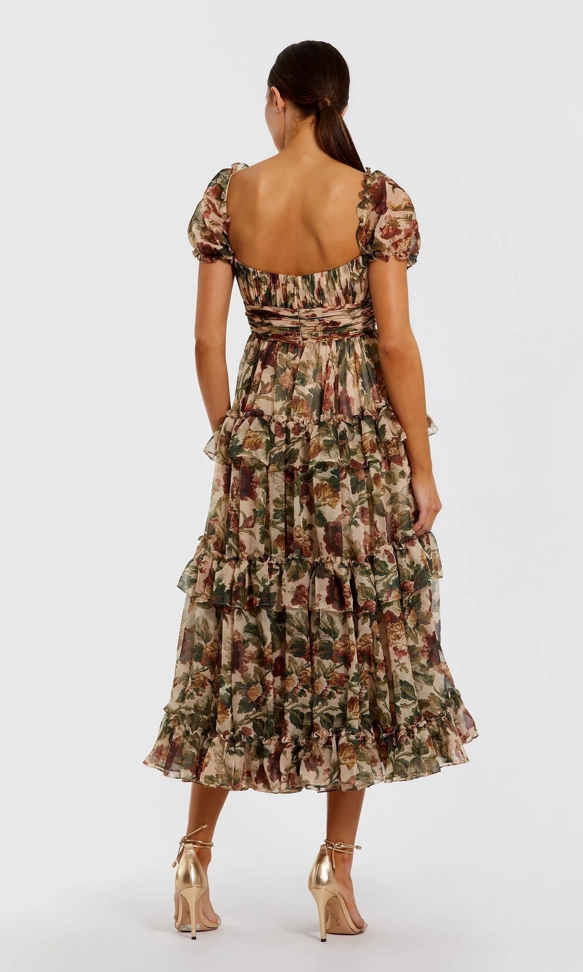A woman faces away in the Mac Duggal 69029 Floral Wedding-Guest Dress, featuring ruffled puff sleeves and a square neckline, styled with metallic gold heels—an ideal choice for wedding guests.