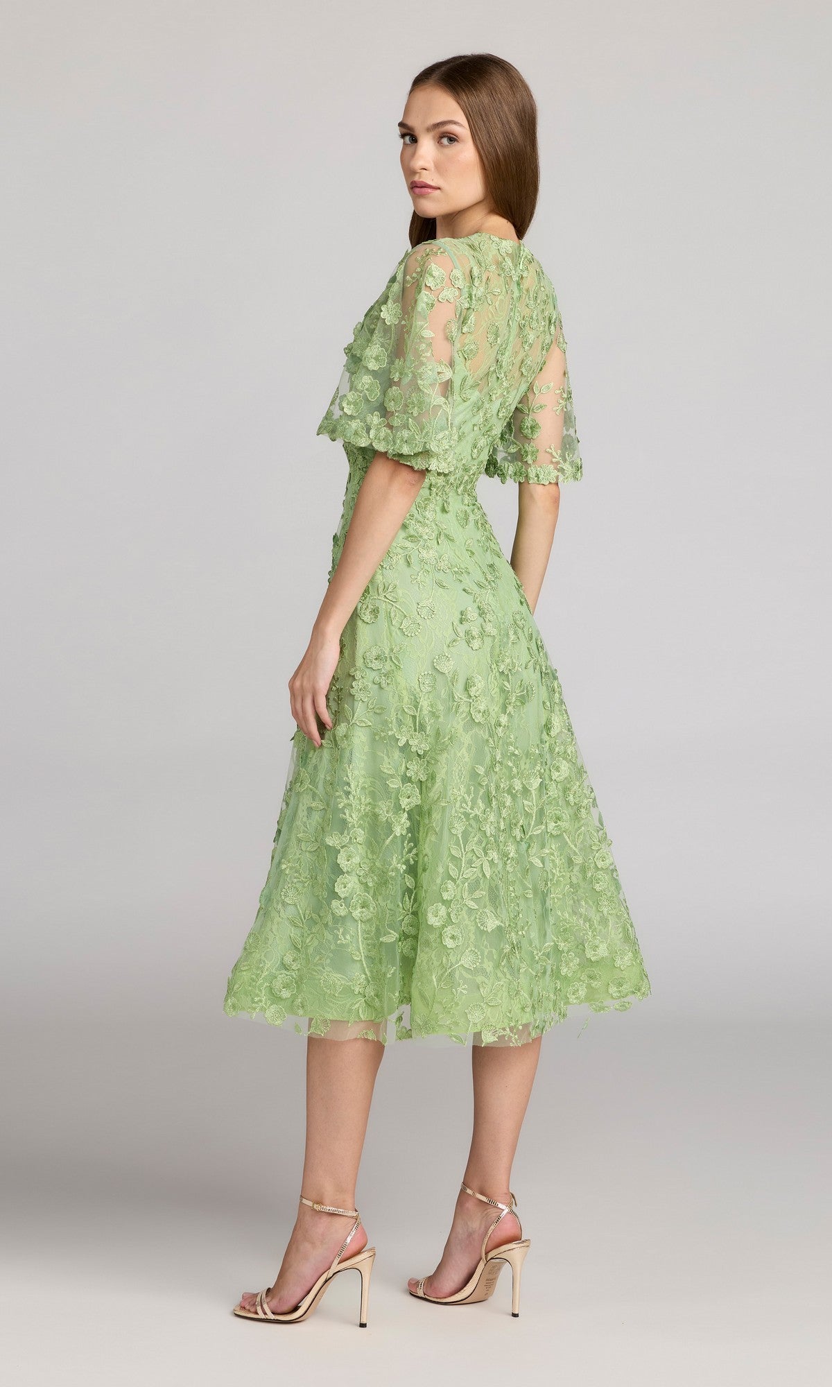 Woman wearing the Mac Duggal 69036 Lace Midi Wedding Guest Dress in light green with floral lace and short sleeves, styled with nude heels, standing against a plain background.