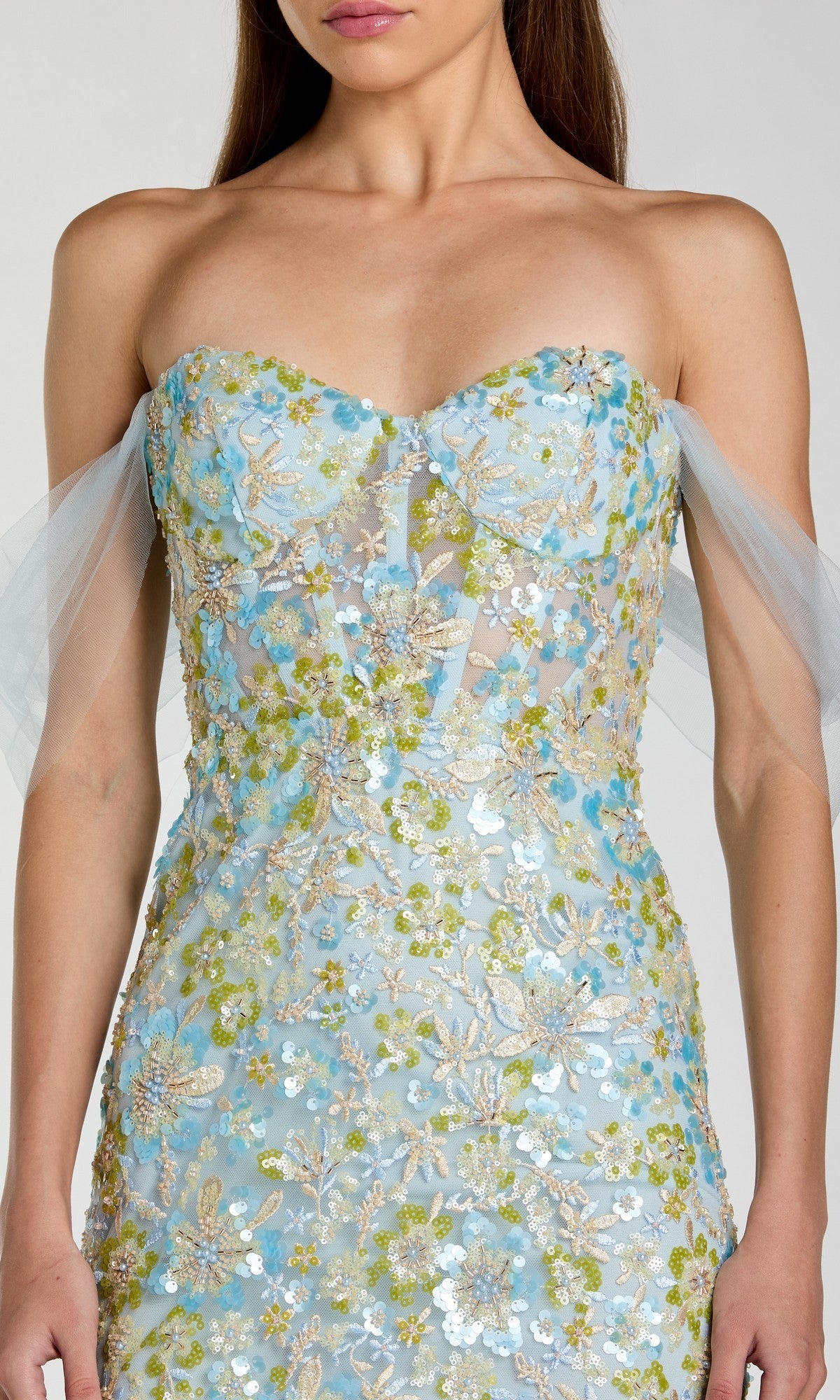 A woman wearing the Mac Duggal 69045 long formal dress, featuring a strapless blue and green floral-embroidered design with sheer off-the-shoulder tulle sleeves, shown from shoulders to hips.