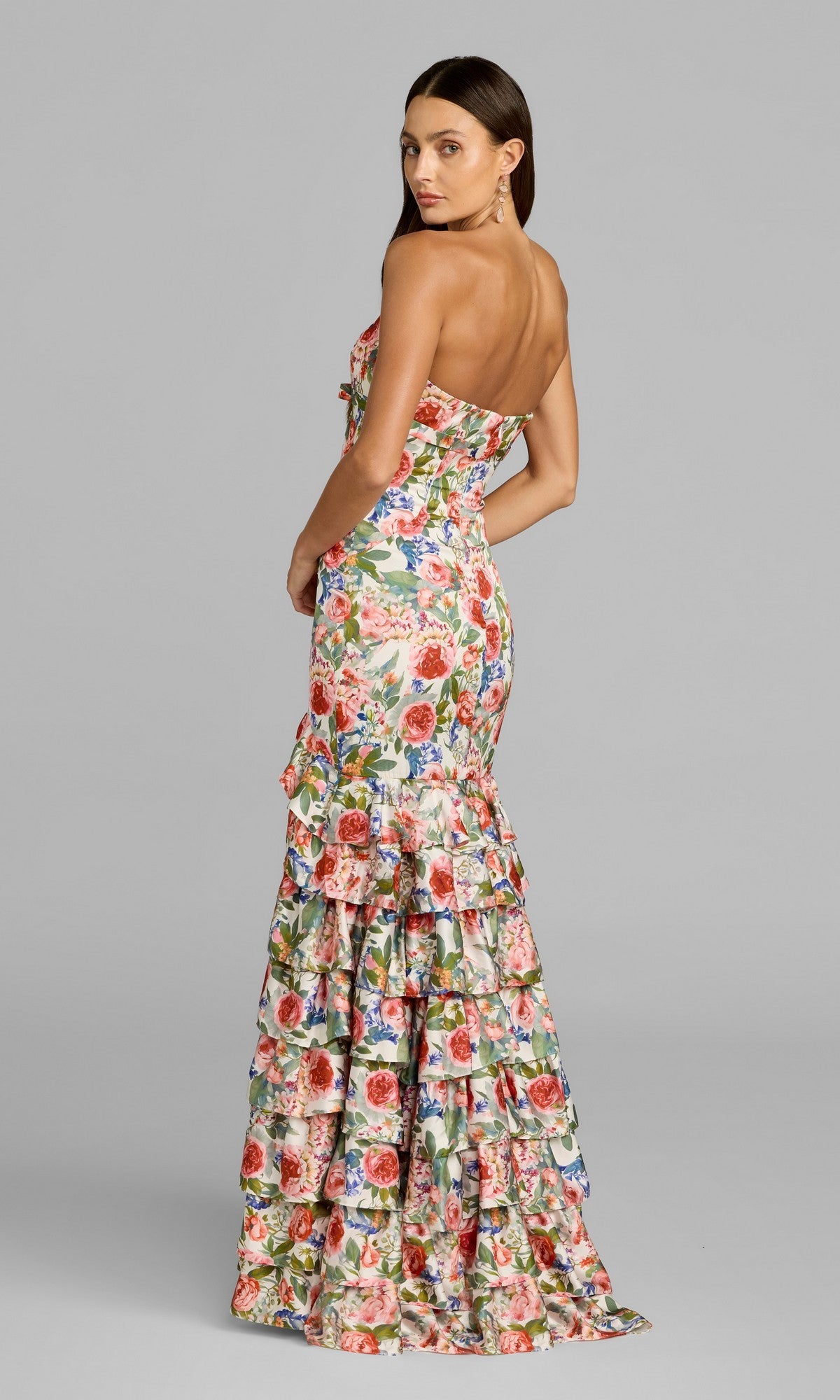 A woman stands facing backward against a plain gray background, wearing the Mac Duggal 69059 Long Formal Dress—a strapless floral gown featuring a fitted bodice and a flared mermaid silhouette, echoing Mac Duggal’s signature style.