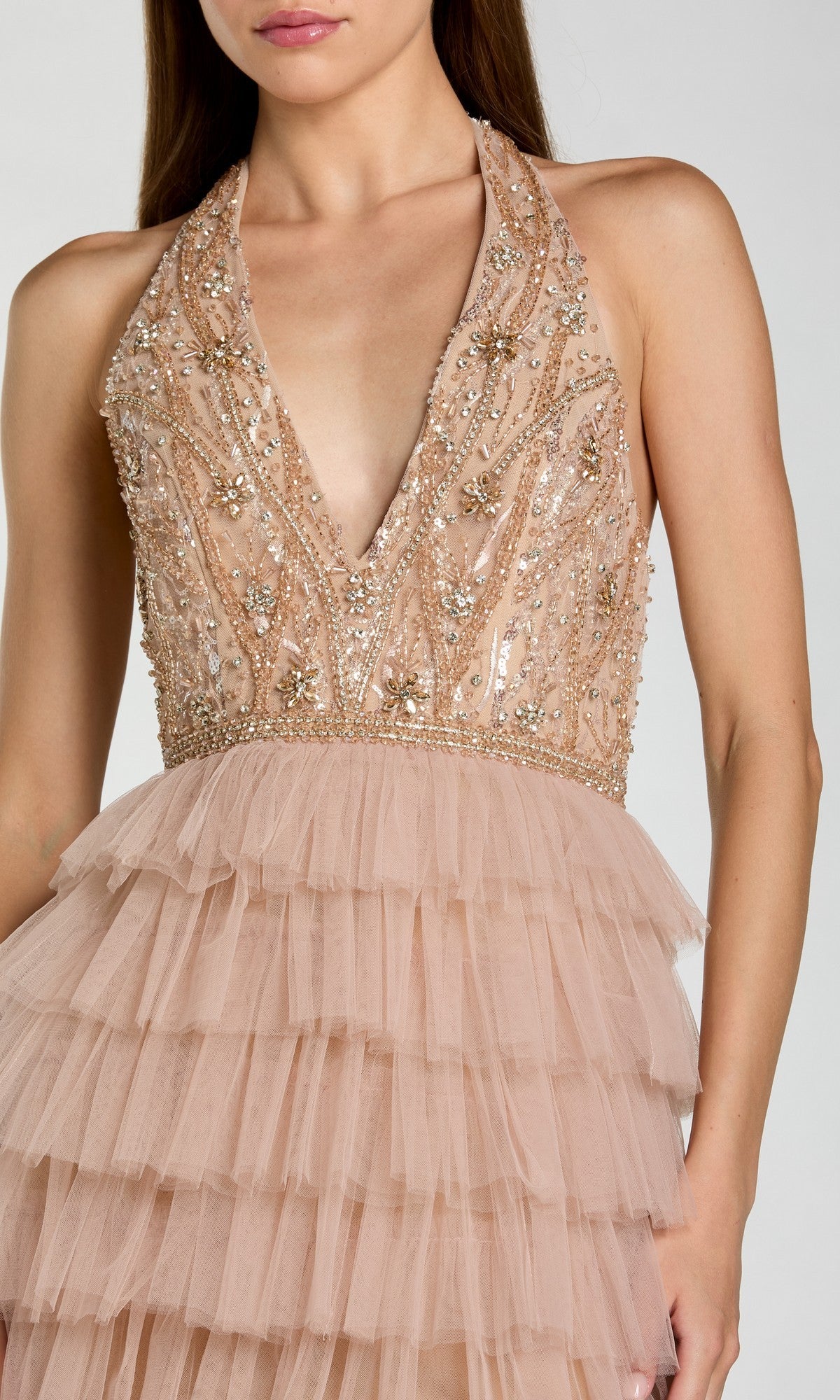 A woman is wearing the Mac Duggal 69062 long formal dress in blush pink, showcasing a sleeveless deep V-neck design with a beaded and sequined bodice, complemented by a layered tulle skirt—an elegant and sophisticated choice for any formal occasion.