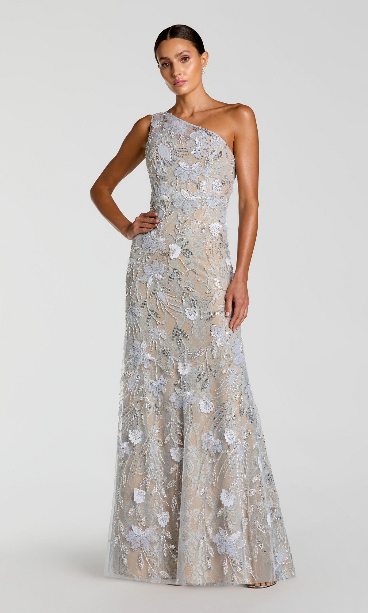 A woman wearing the Long Formal Dress: Mac Duggal 69077 in powder blue—a floor-length, one-shoulder gown adorned with delicate silver floral lace embroidery over a nude underlay—stands against a plain light background.
