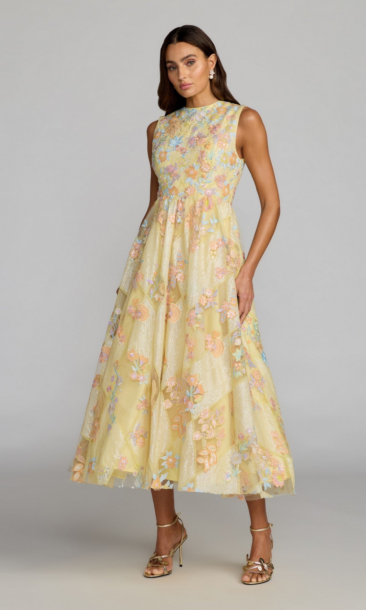 A woman wearing the Mac Duggal 69111 Tea-Length Party Dress in Yellow Multi, featuring colorful floral embroidery, stands against a neutral background.