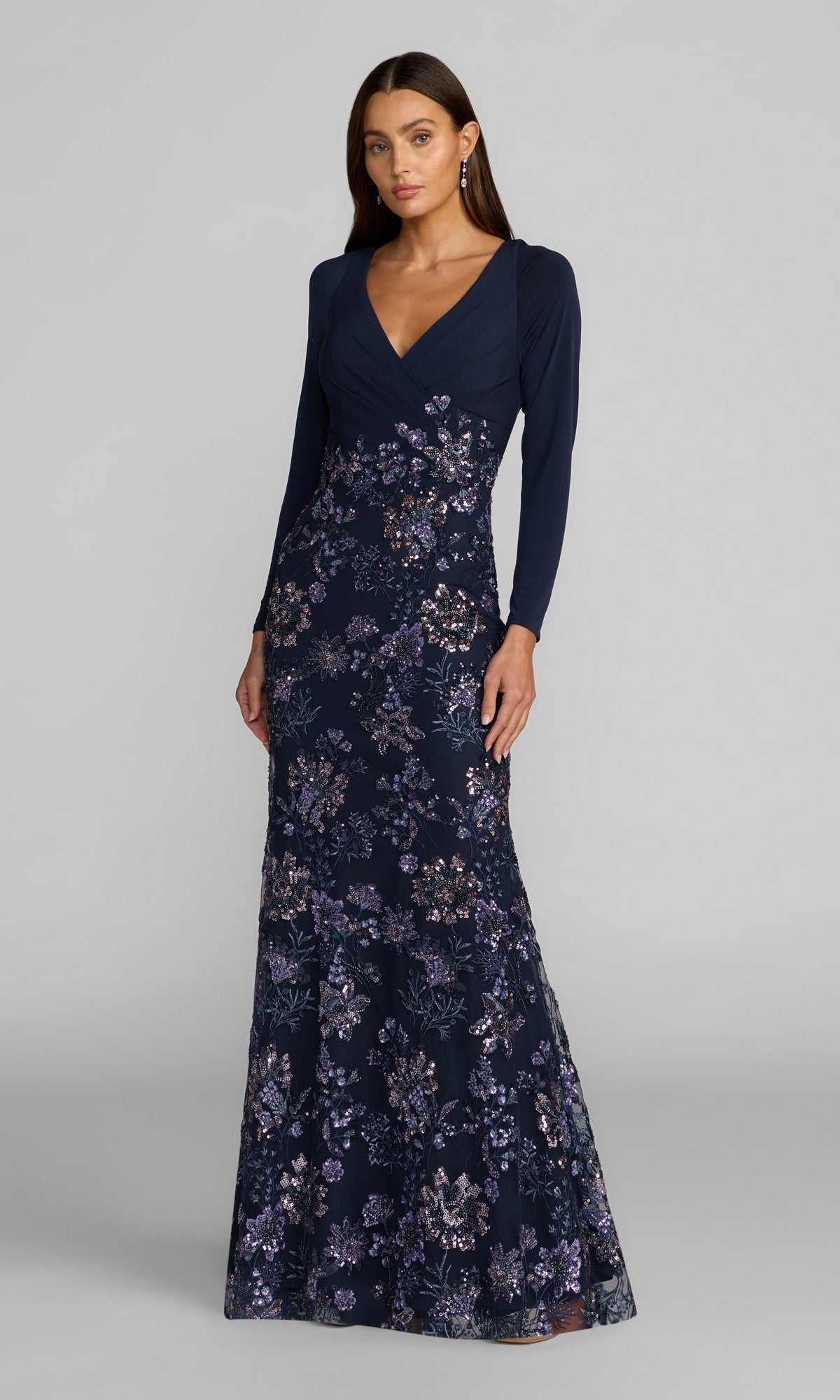 A woman wearing the Mac Duggal 69122 long formal dress in Midnight Multi, featuring long sleeves and intricate sequin floral embroidery, stands against a plain gray background. This modest formal dress flatters her figure and offers an elegant, timeless look.