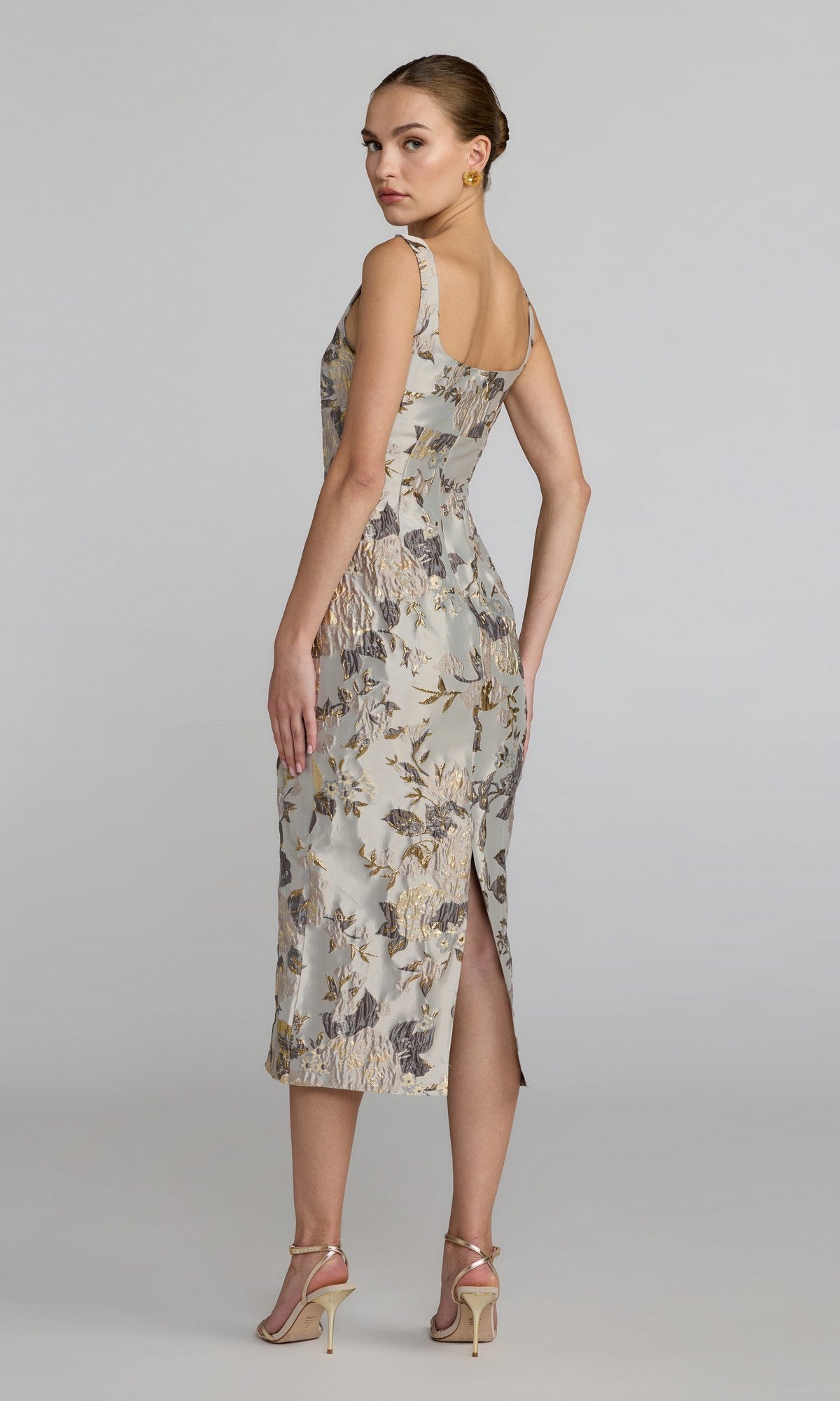 Woman standing in a three-quarter pose wears the Floral Midi Wedding Guest Dress: Mac Duggal 69152—a light-colored, floral midi dress featuring a back slit—paired with strappy high-heeled sandals against a plain background. Perfect for weddings or special occasions, this elegant look channels the timeless charm of the Mac Duggal 69152 style.
