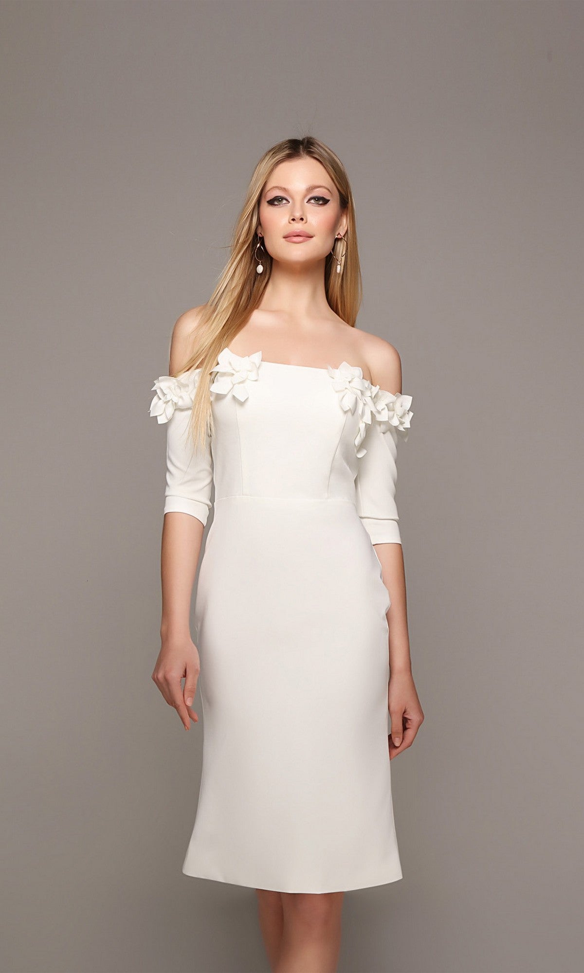 A woman models the Alyce 70003 knee-length semi-formal dress with off-the-shoulder sleeves and delicate 3D floral appliques along the neckline, set against a plain gray background.