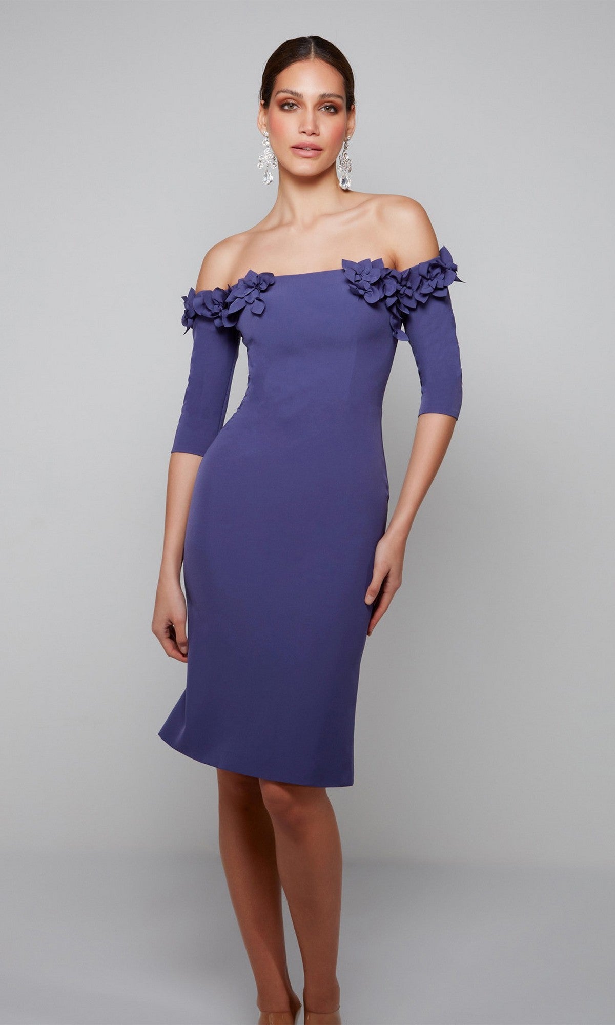 A woman models the Alyce 70003 knee-length semi-formal dress in Storm Cloud, featuring off-the-shoulder sleeves and 3D floral appliques on the neckline, against a plain gray background.