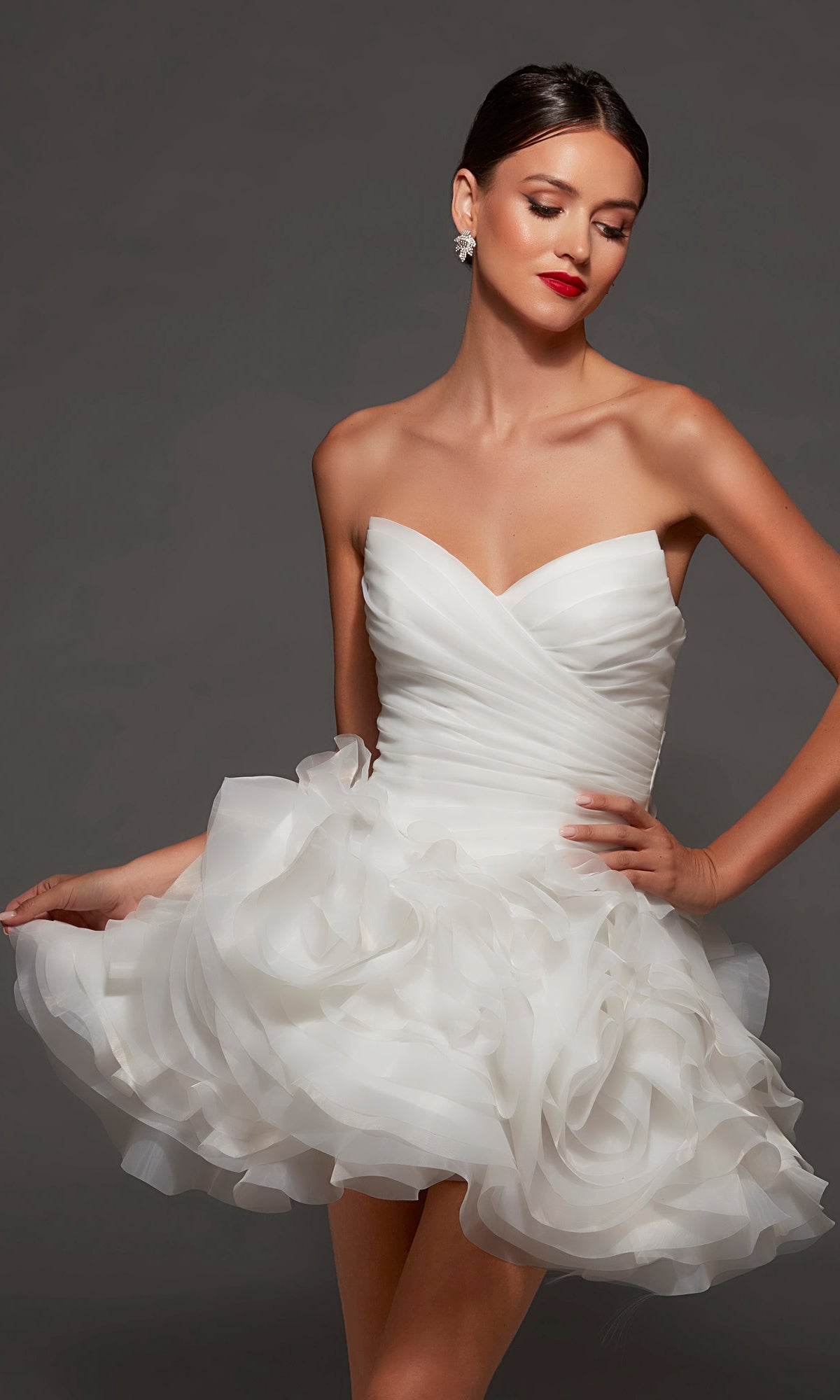 A woman wears the Alyce 70086 Short White Party Dress in Diamond White, featuring a strapless sweetheart neckline, fitted bodice, and layered ruffled mini skirt, while posing against a dark background.