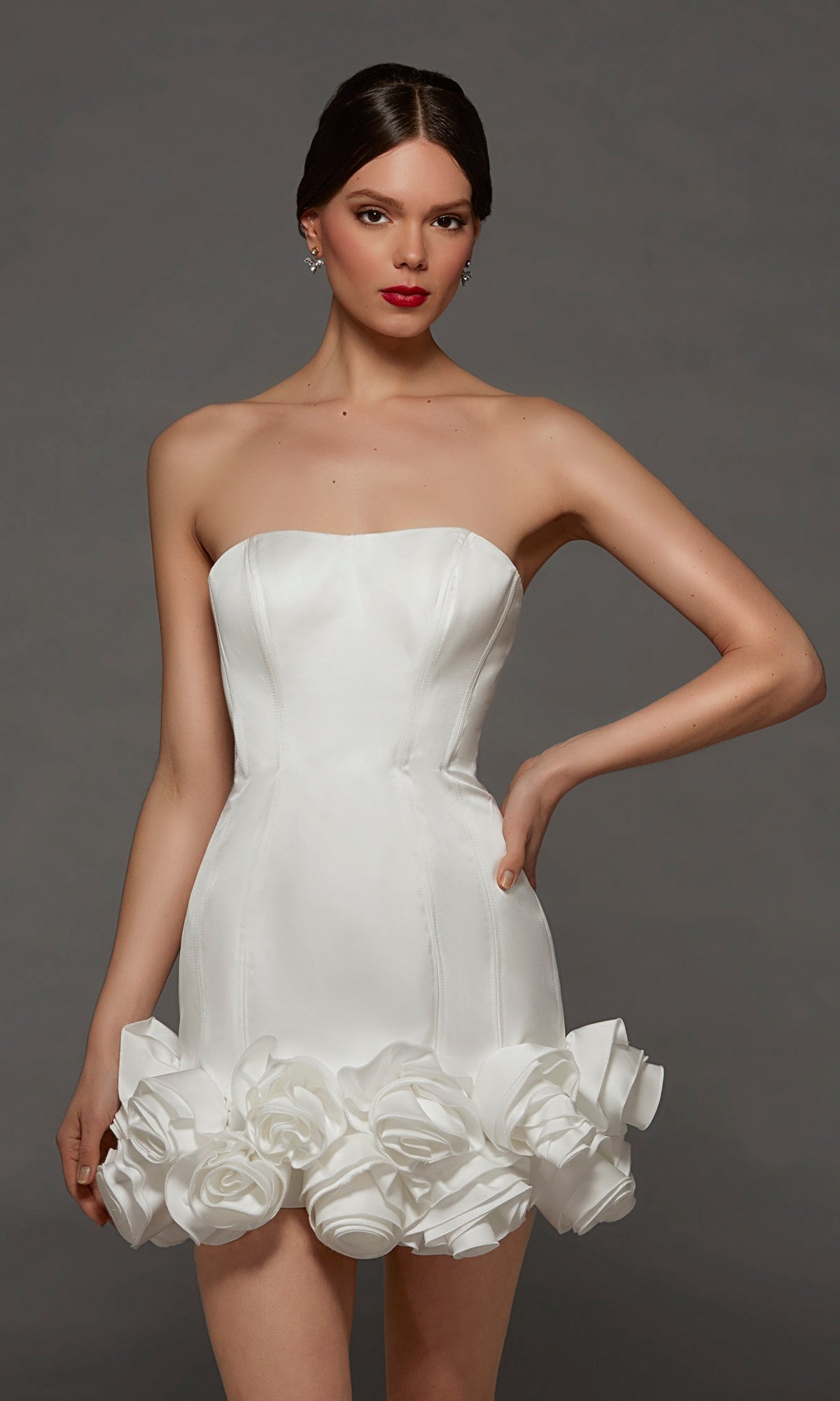 A woman stands against a plain gray background wearing the Alyce 70087 short white party dress, a strapless bodycon style adorned with sculpted rose details along the rosette hemline.