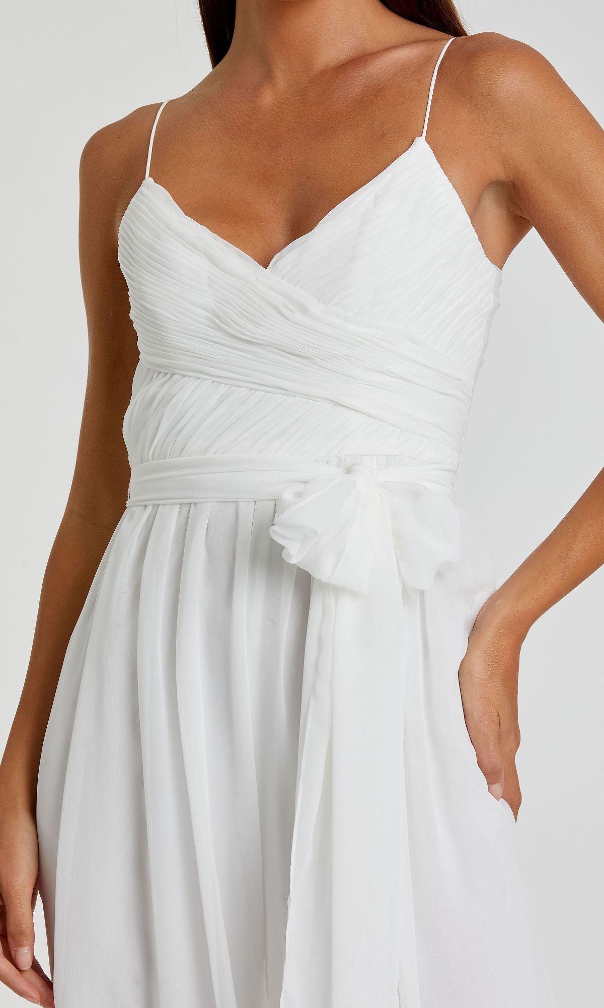 A woman wears the Mac Duggal 70100 Flowing Wide-Leg Formal Jumpsuit, featuring a sleeveless white design with thin straps, a V-neckline, ruched bodice, and fabric belt at the waist.