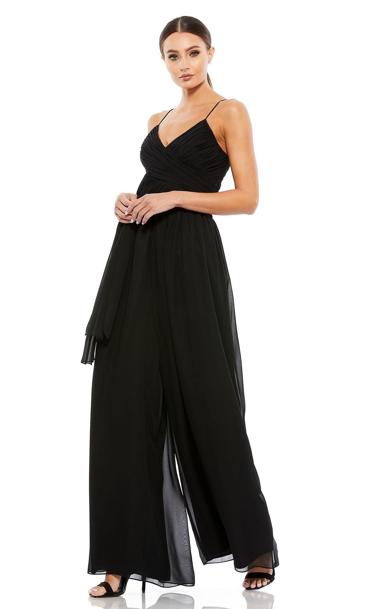 A woman in the Mac Duggal 70100 Flowing Wide-Leg Formal Jumpsuit, featuring a sleeveless black design with crossover bodice and spaghetti straps, stands against a plain white background.