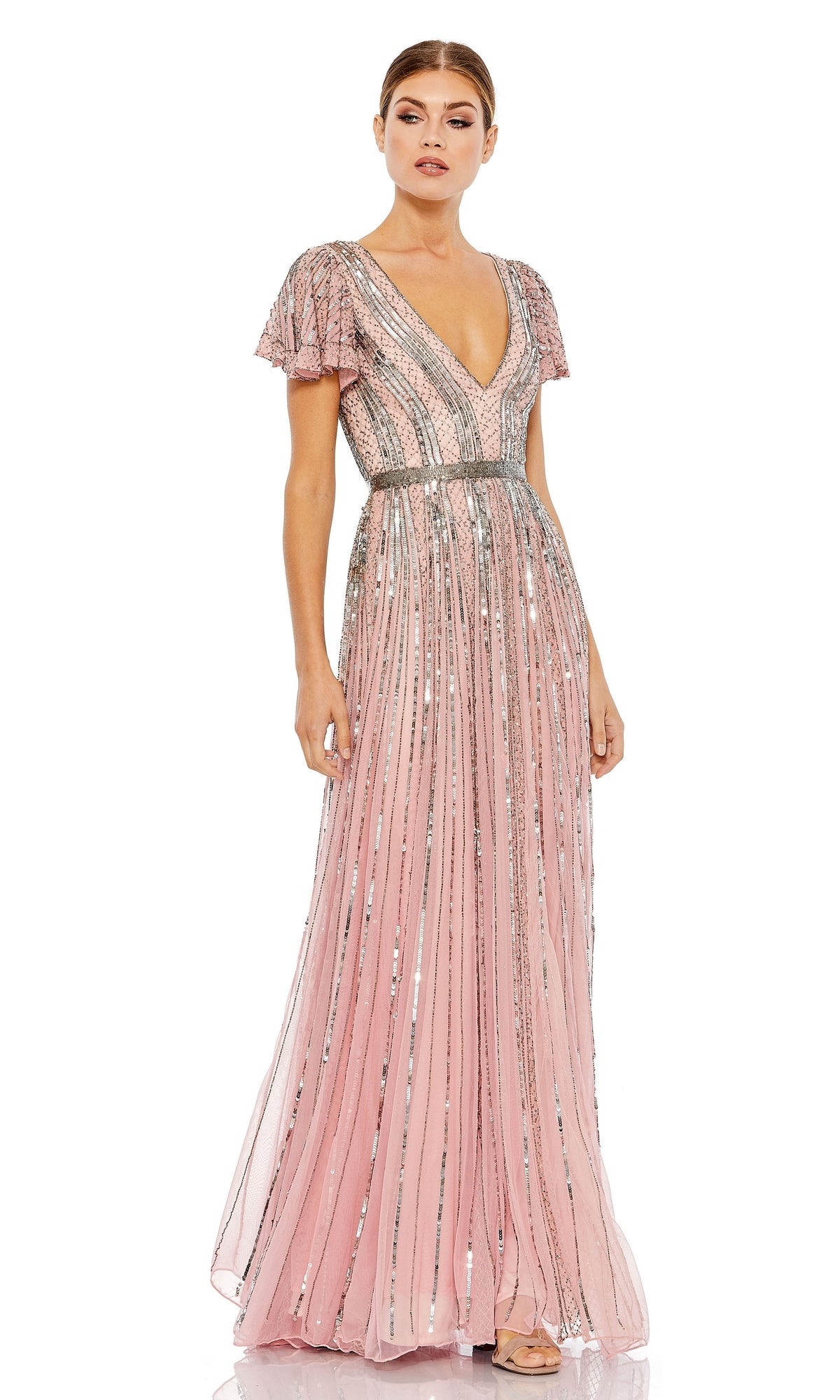 A woman stands wearing the Long Formal Dress 70108 by Mac Duggal—a floor-length pink sequin A-line gown with silver embellishments, short flutter sleeves, and a V-neckline.
