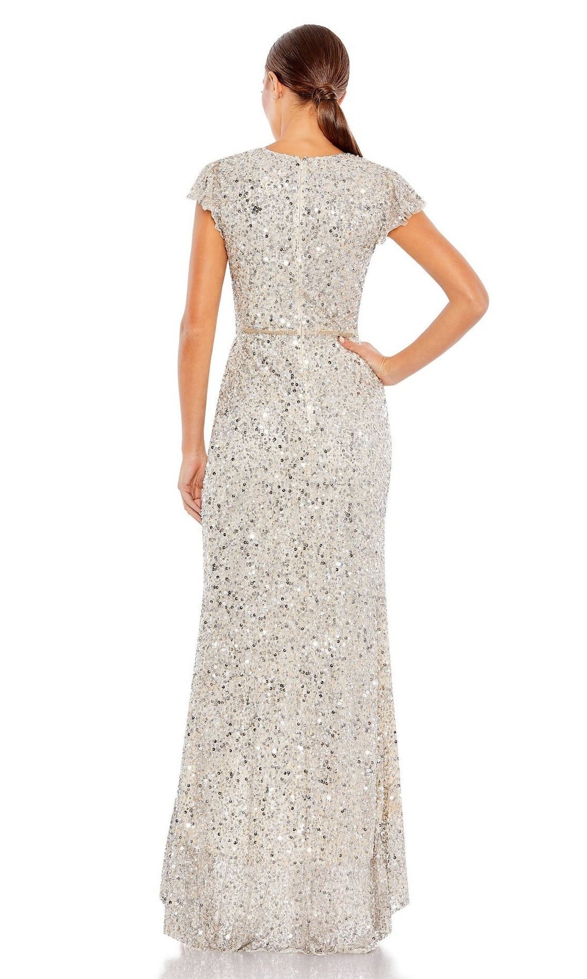 A woman models the Mac Duggal Long Formal Dress 70113—floor-length, short-sleeved, silver sequins with a v-neckline—standing facing away with one hand on her hip.