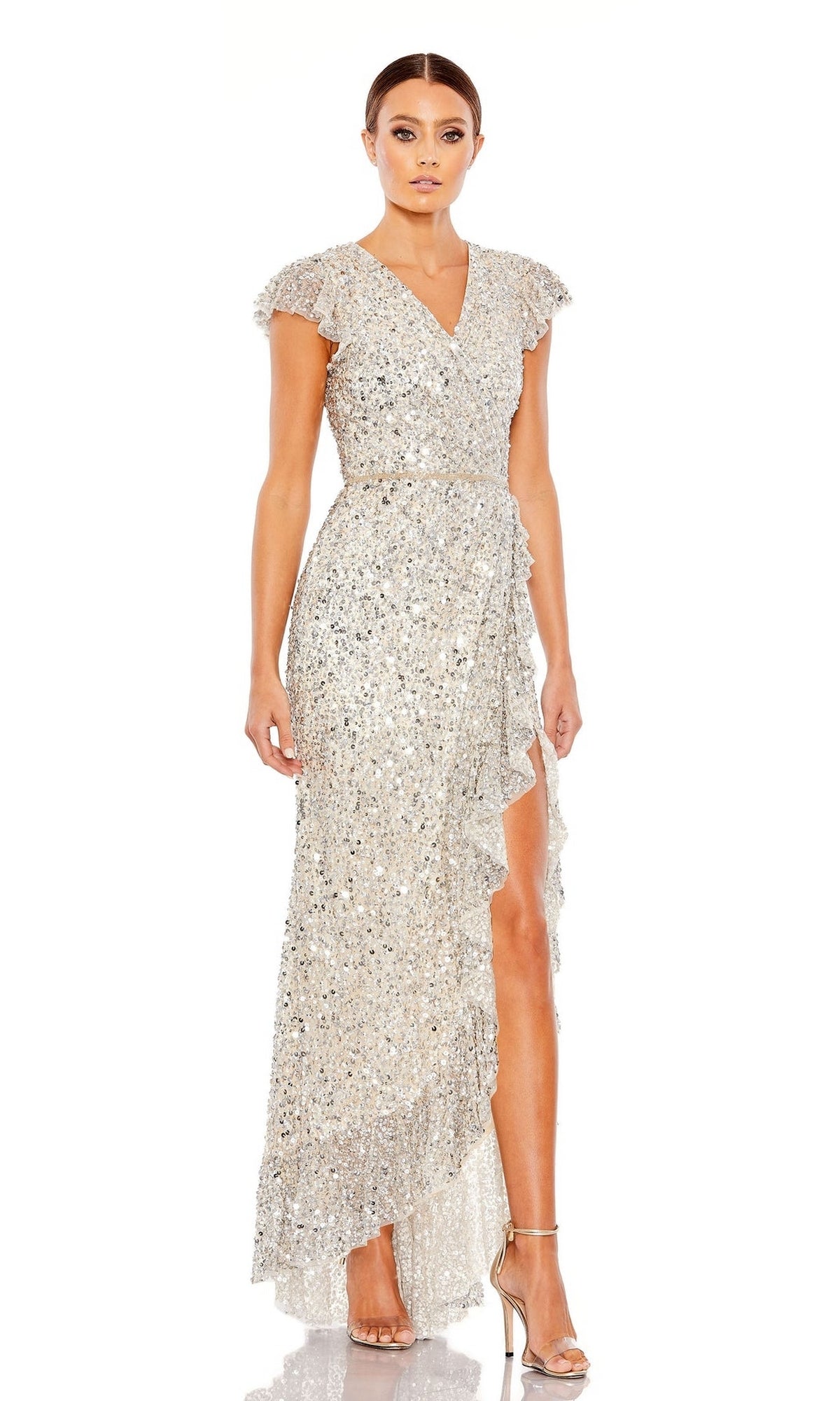 A woman models the Long Formal Dress 70113 by Mac Duggal, featuring silver sequins, a v-neckline, short flutter sleeves, and a ruffled high-low hem, paired with strappy heels against a plain white background.