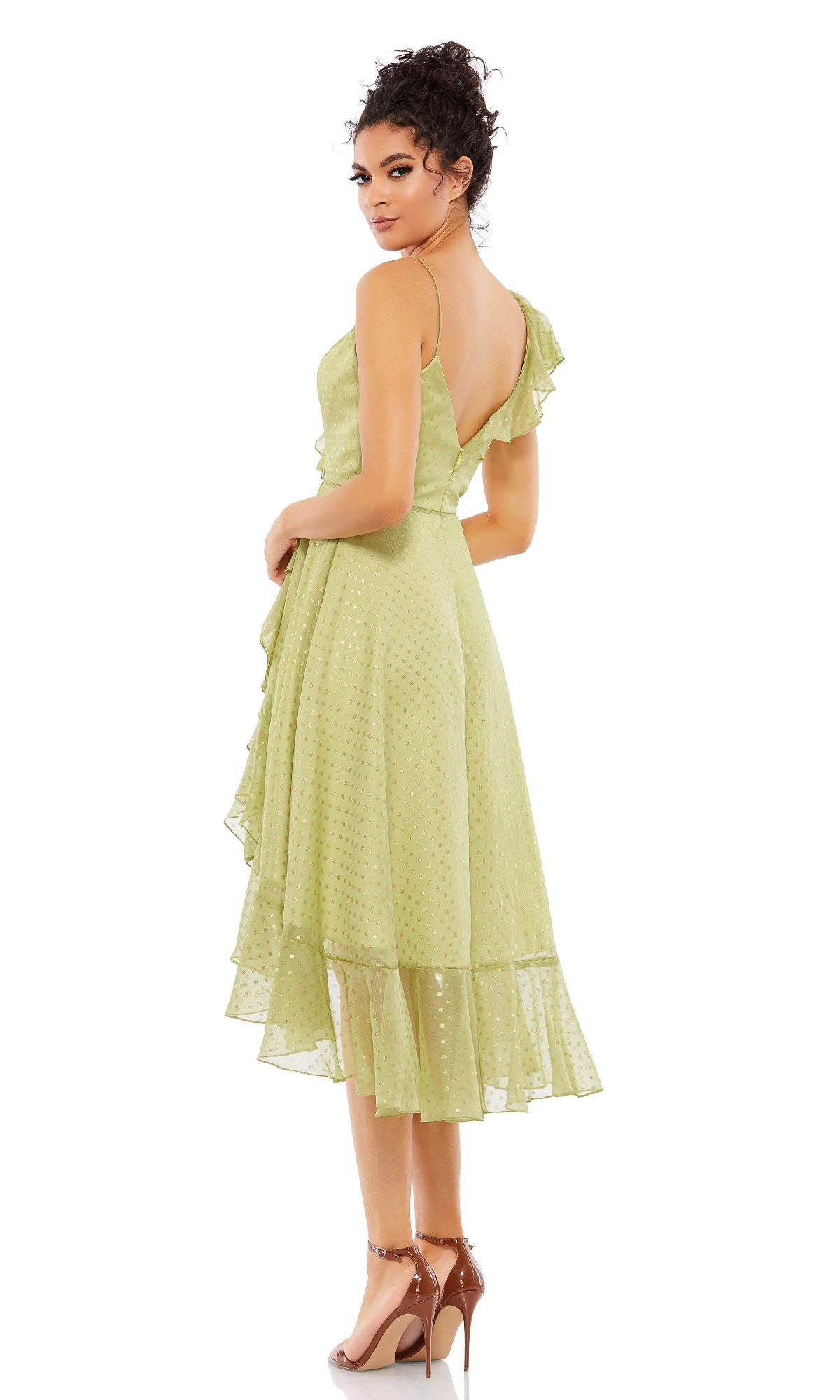 A woman in the Mac Duggal 70163 short green wedding guest dress with asymmetrical ruffles and tan high-heeled sandals stands facing away, glancing over her shoulder.