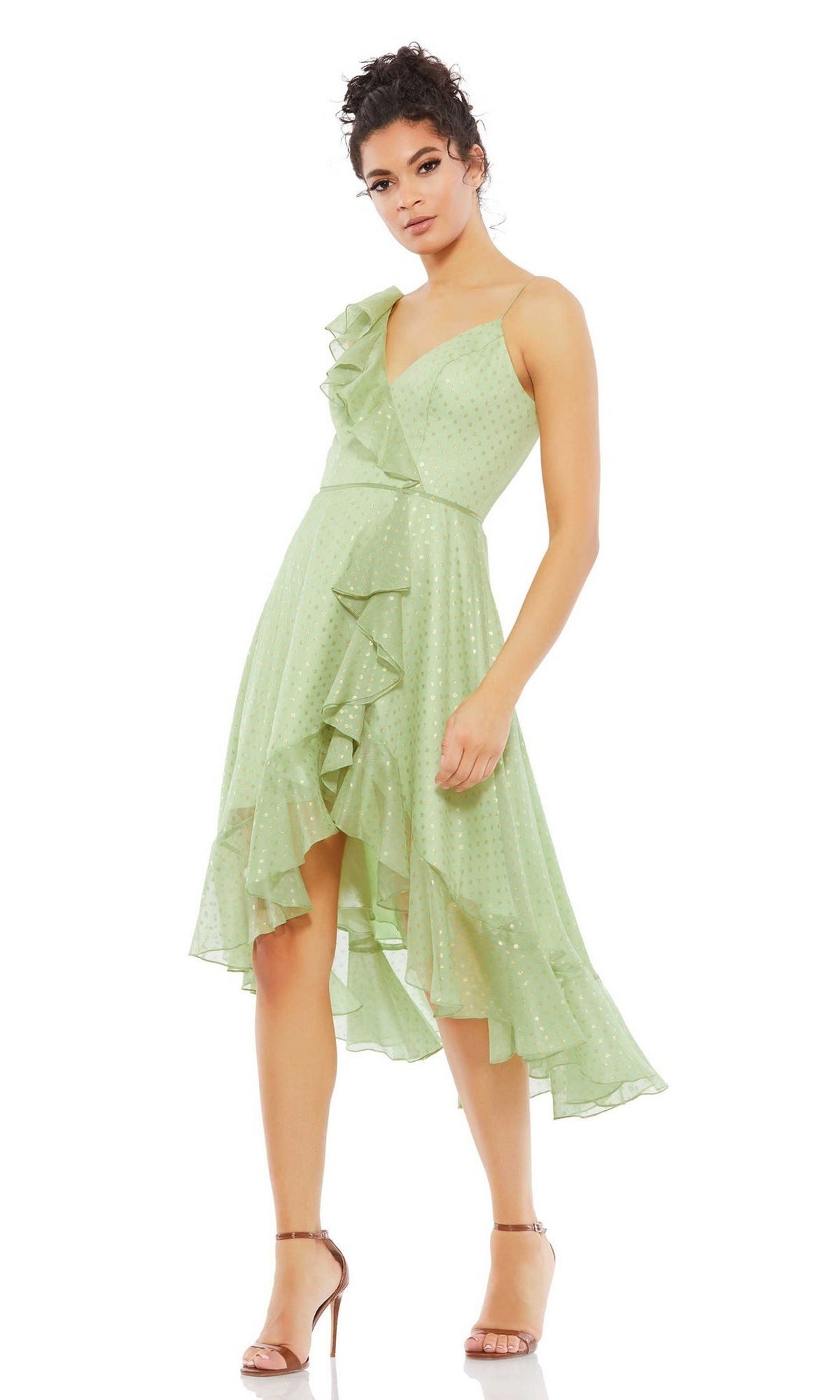 A woman stands against a plain white background wearing the Mac Duggal 70163 short green wedding guest dress with ruffle details and gold polka dots, styled with strappy nude heels.