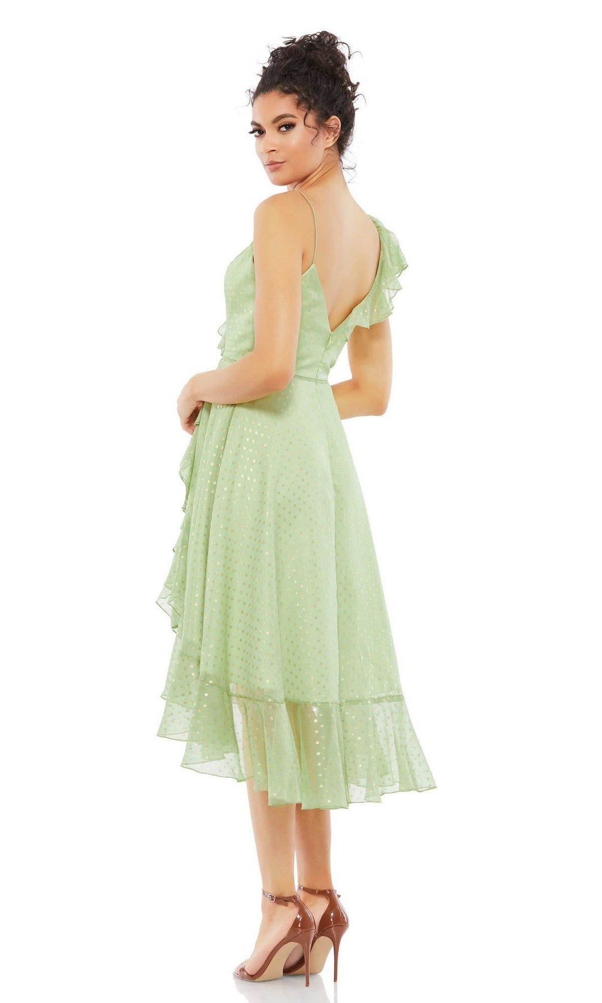 A woman in the Mac Duggal 70163 short green wedding guest dress with ruffles and gold polka dots, paired with nude heels, stands against a white background, looking over her shoulder.