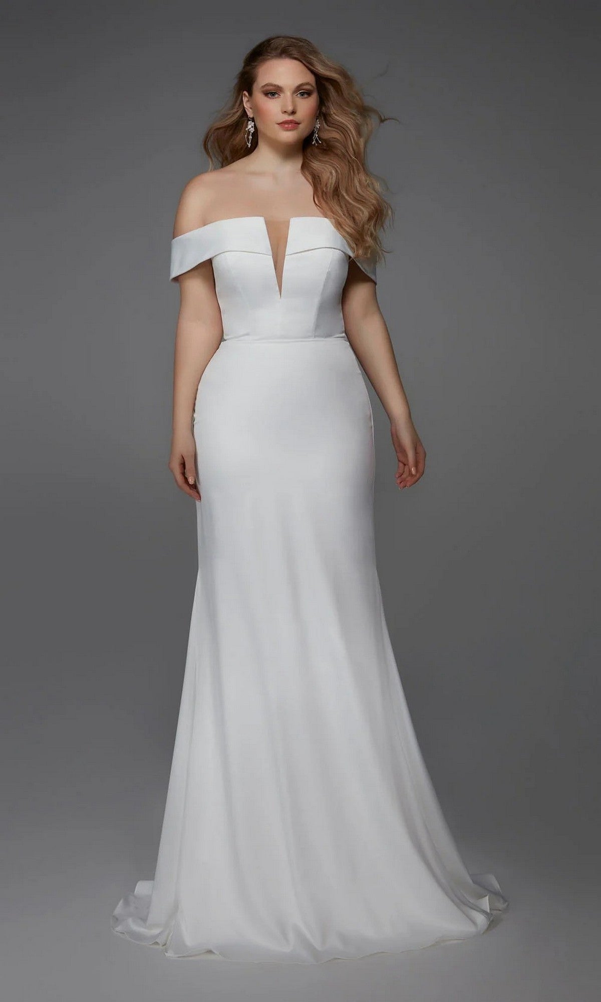 A woman models the Alyce 7020 Long White Dress—a satin, off-the-shoulder, floor-length gown with a fitted bodice and deep V-neckline—against a plain gray background, ideal for bridal events or elegant wedding receptions.