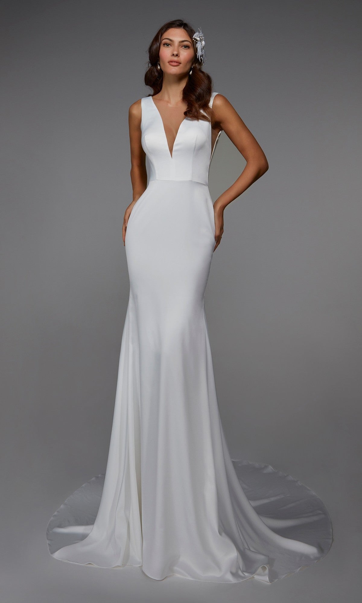 A woman models the Alyce 7021 long formal dress, a sleeveless white gown with a plunging V-neckline and subtle train, standing against a plain gray background.