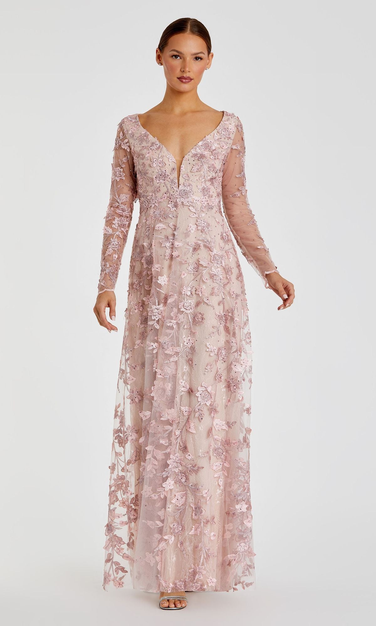 A woman stands facing forward in the Mac Duggal 70224 Long Sleeve Long Formal Dress—a light pink, embroidered maxi gown with floral details—set against a plain white background.