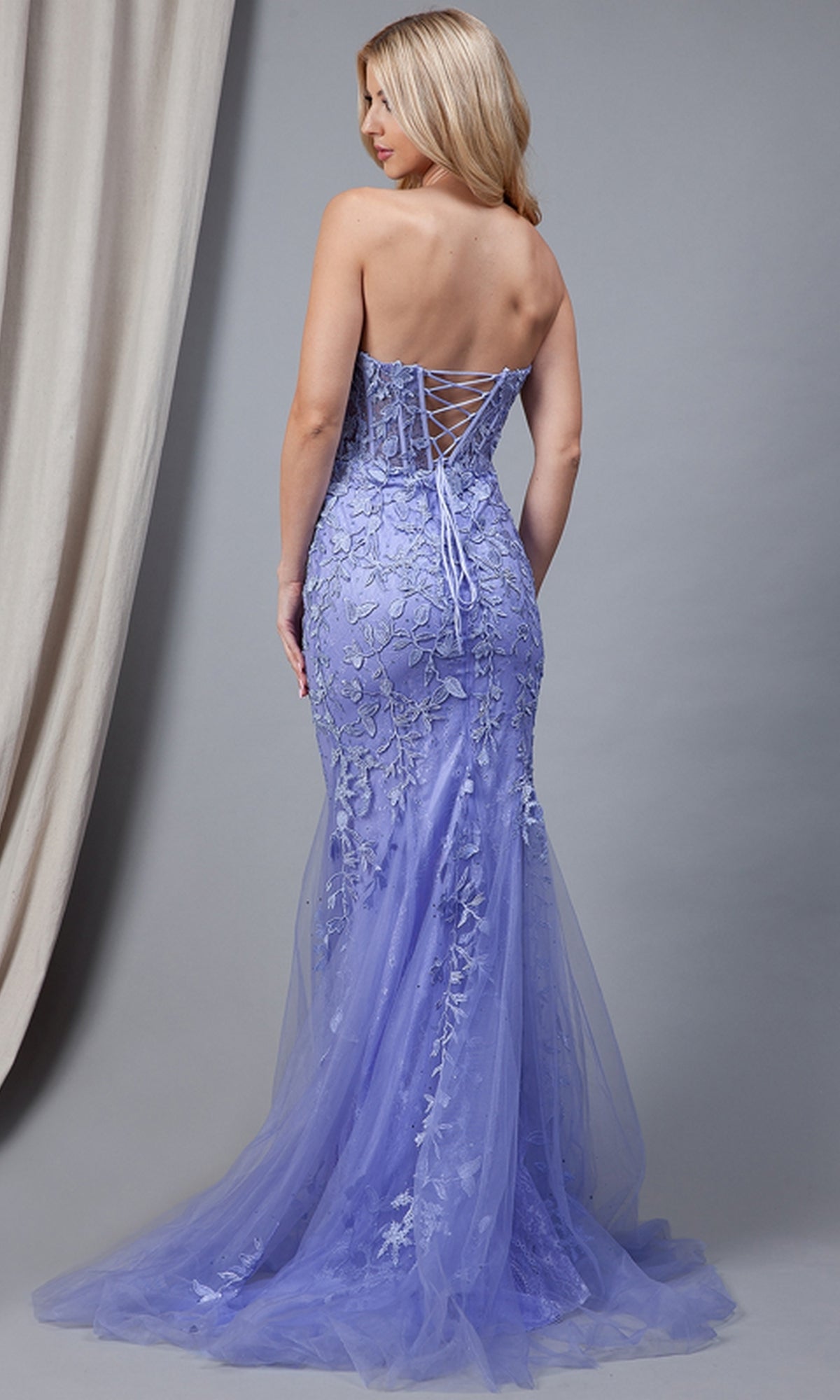 A woman in the Strapless Sweetheart Long Mermaid Prom Dress 7024, featuring a strapless bodice and embroidered floral details, stands facing away against a gray backdrop.