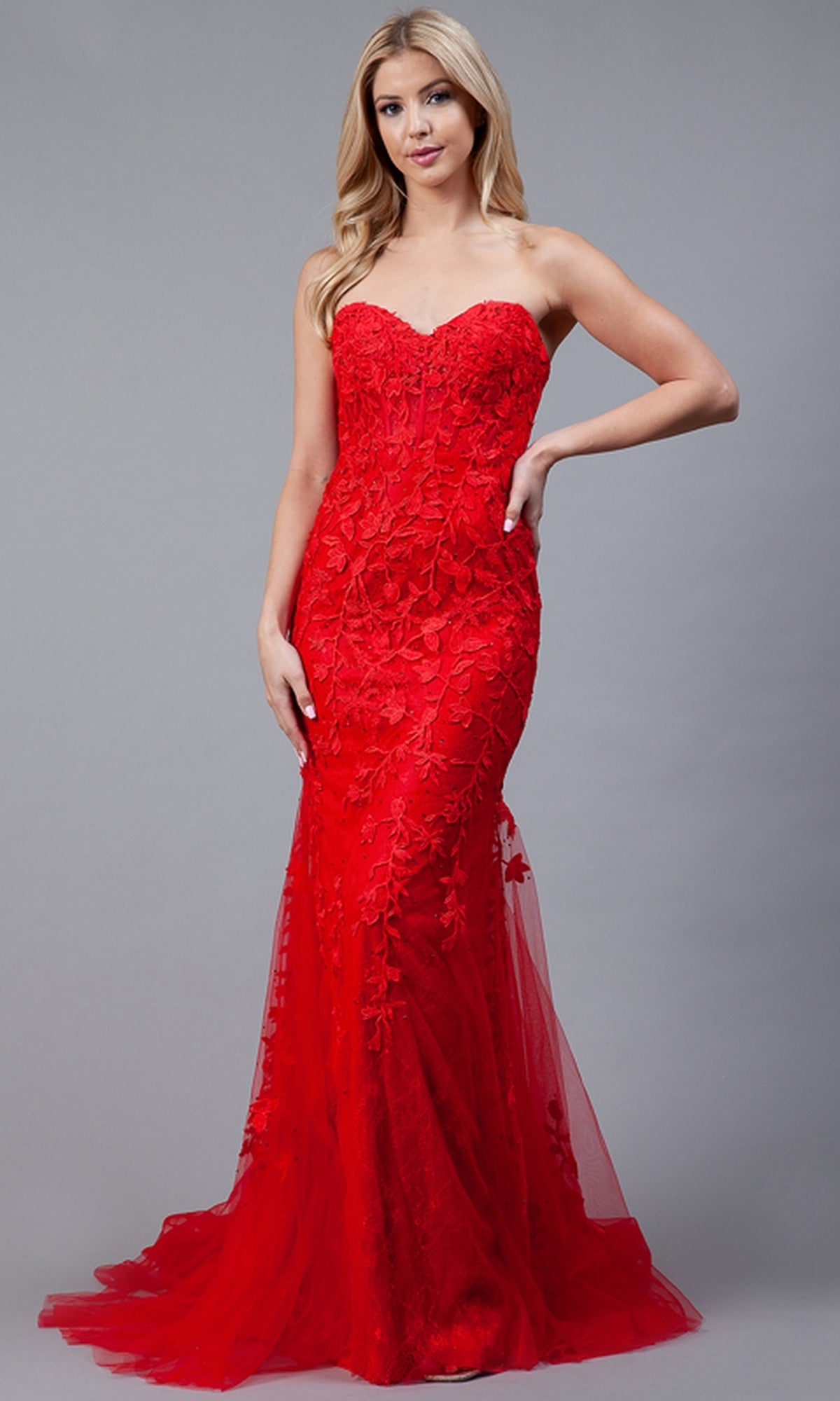 A woman models the Strapless Sweetheart Long Mermaid Prom Dress 7024 in red, featuring lace and embroidered floral designs, against a plain gray background.