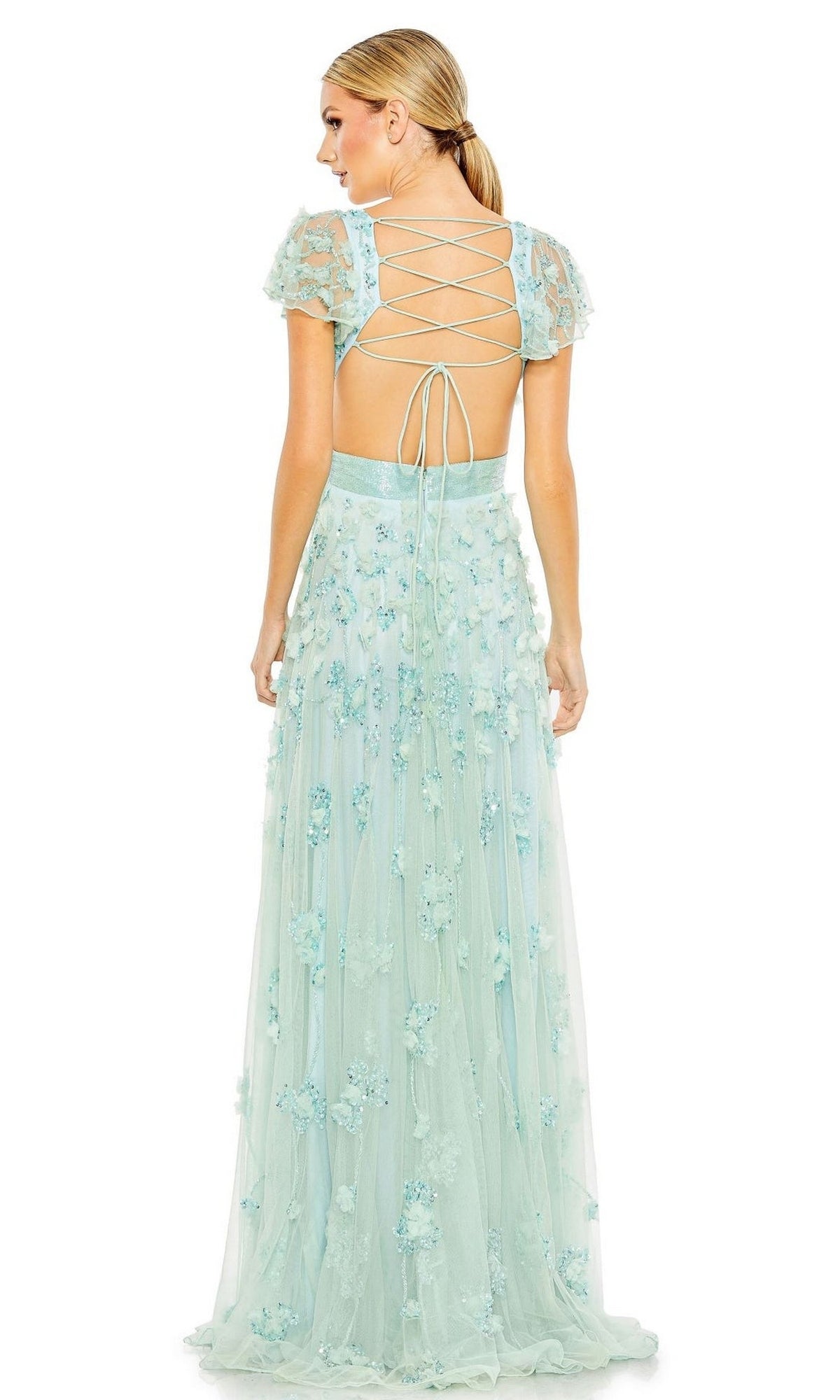 A woman stands facing away in the Long Formal Dress 70275 by Mac Duggal, a light blue A-line gown featuring floral embellishments, sheer short sleeves, and a lace-up open back.