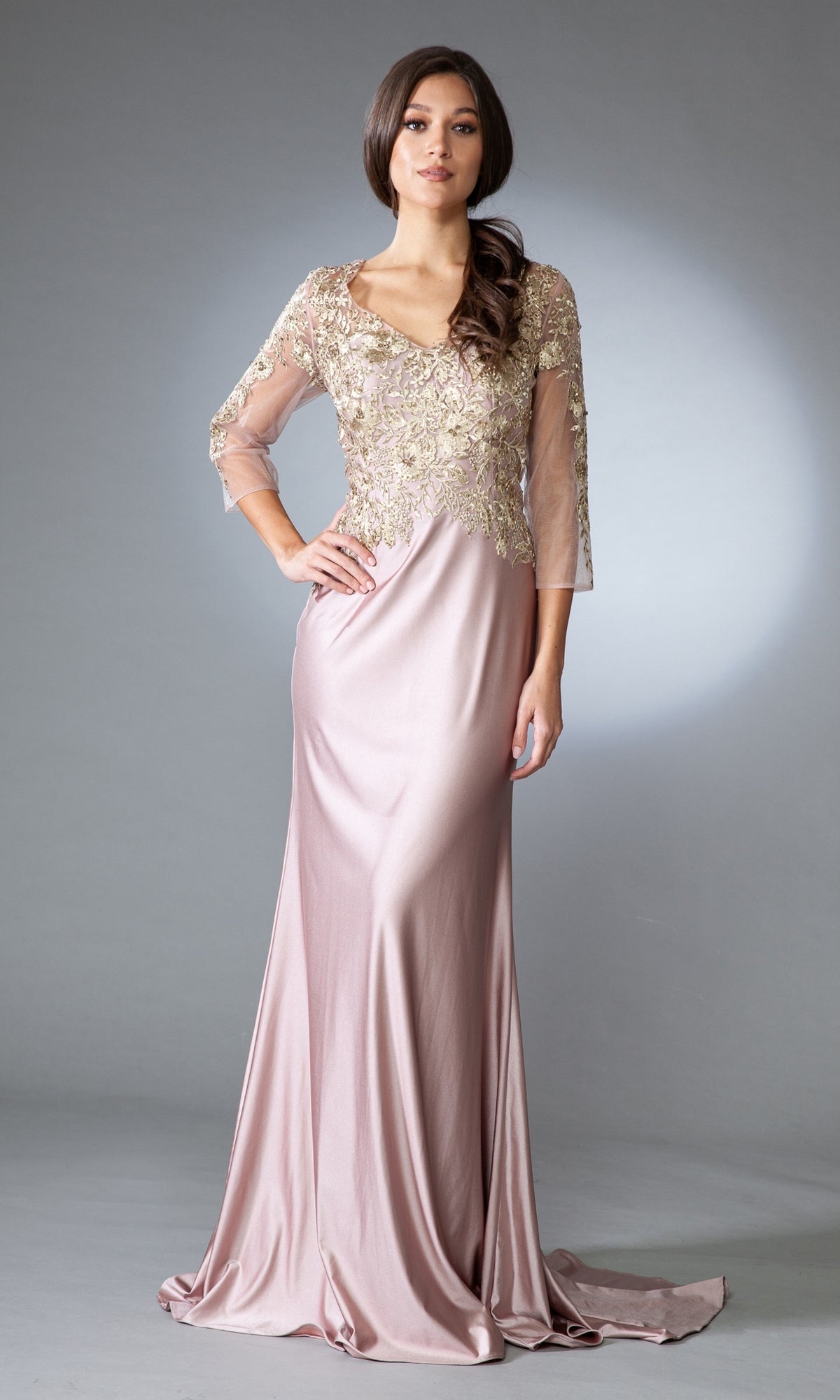 A woman wears the Amelia Couture 7039, a floor-length pale pink gown with sheer long sleeves and an embroidered bodice—an elegant mother-of-the-bride dress.