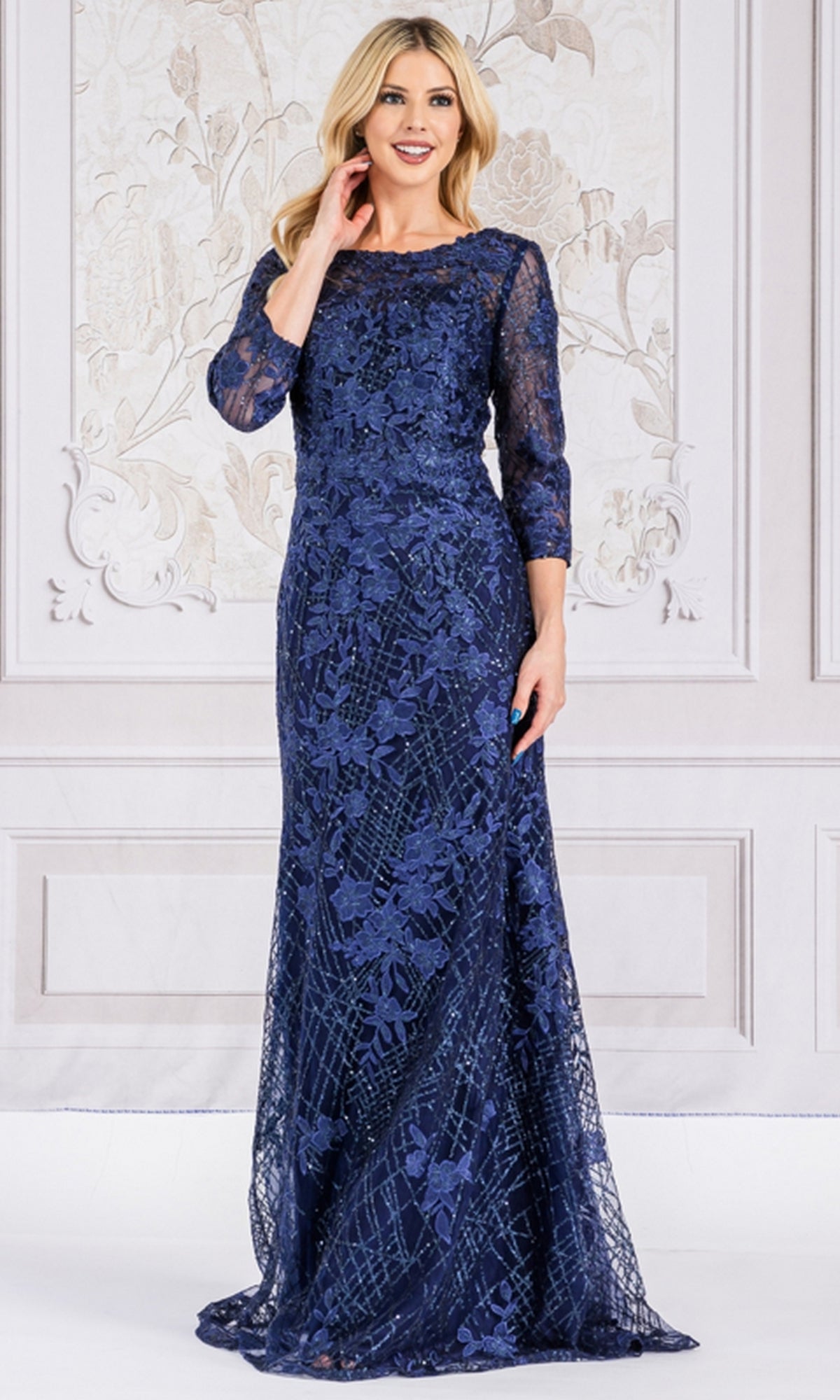 A woman stands indoors wearing the Floral-Embroidered Long Sleeve Formal Dress 7045, a floor-length navy gown with elegant floral embroidery.