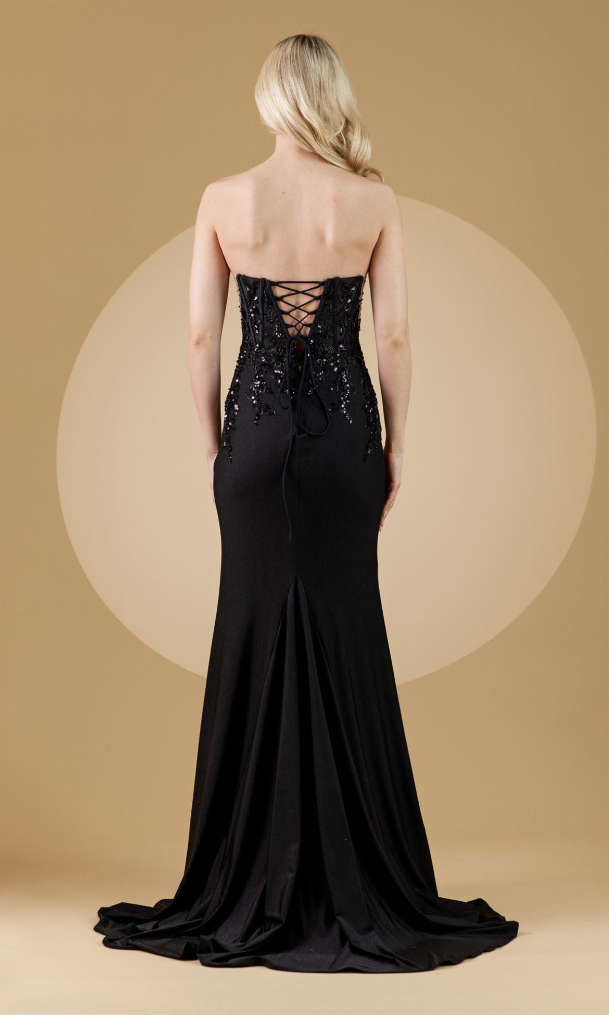 A blonde woman models the Strapless Sweetheart Sheer-Sides Long Prom Dress 7052, featuring a lace-up back and floor-length, slightly flared hem, standing against a solid beige background.