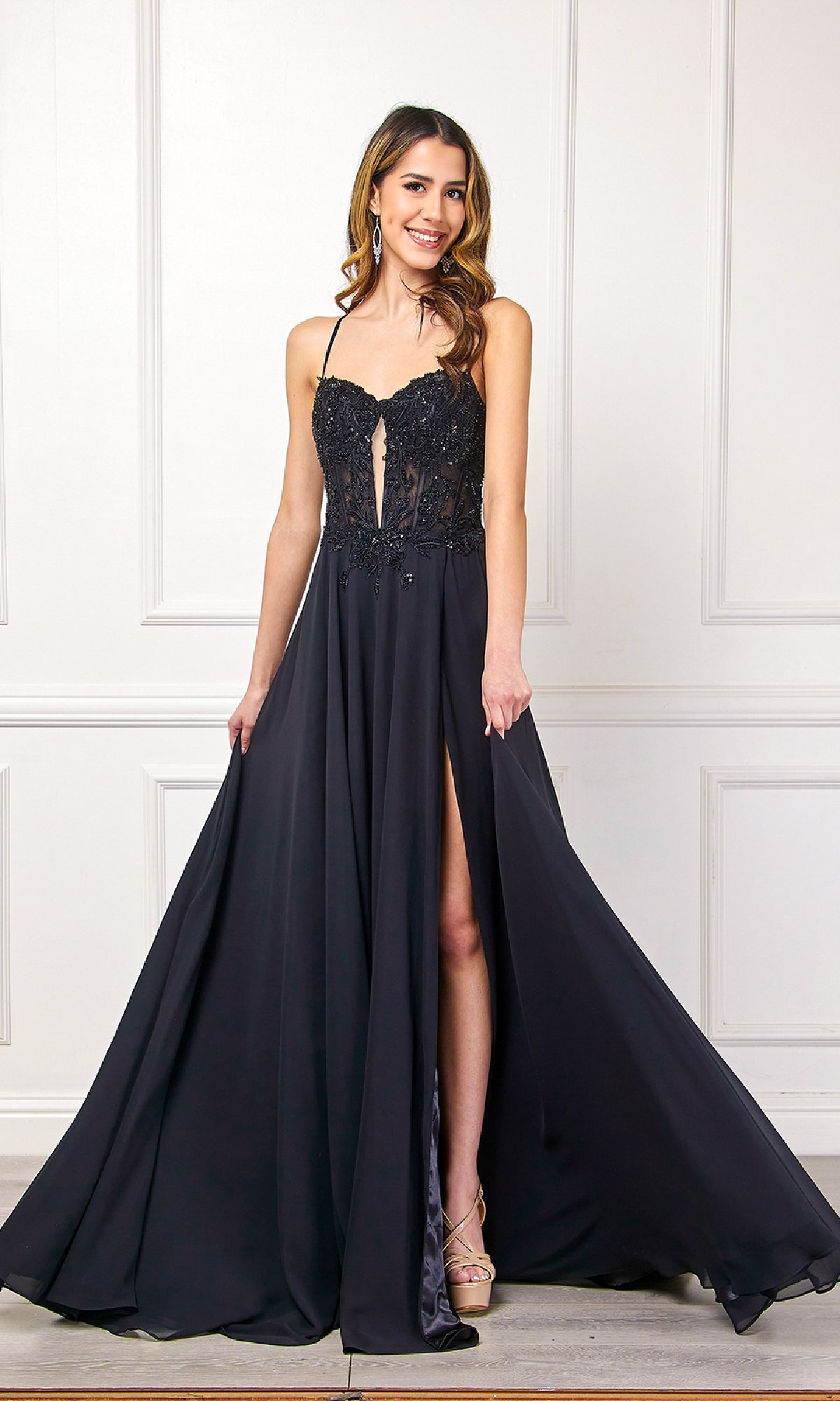 Woman wearing the Amelia Couture 7066 long black corset prom dress, posing in front of a white paneled wall.