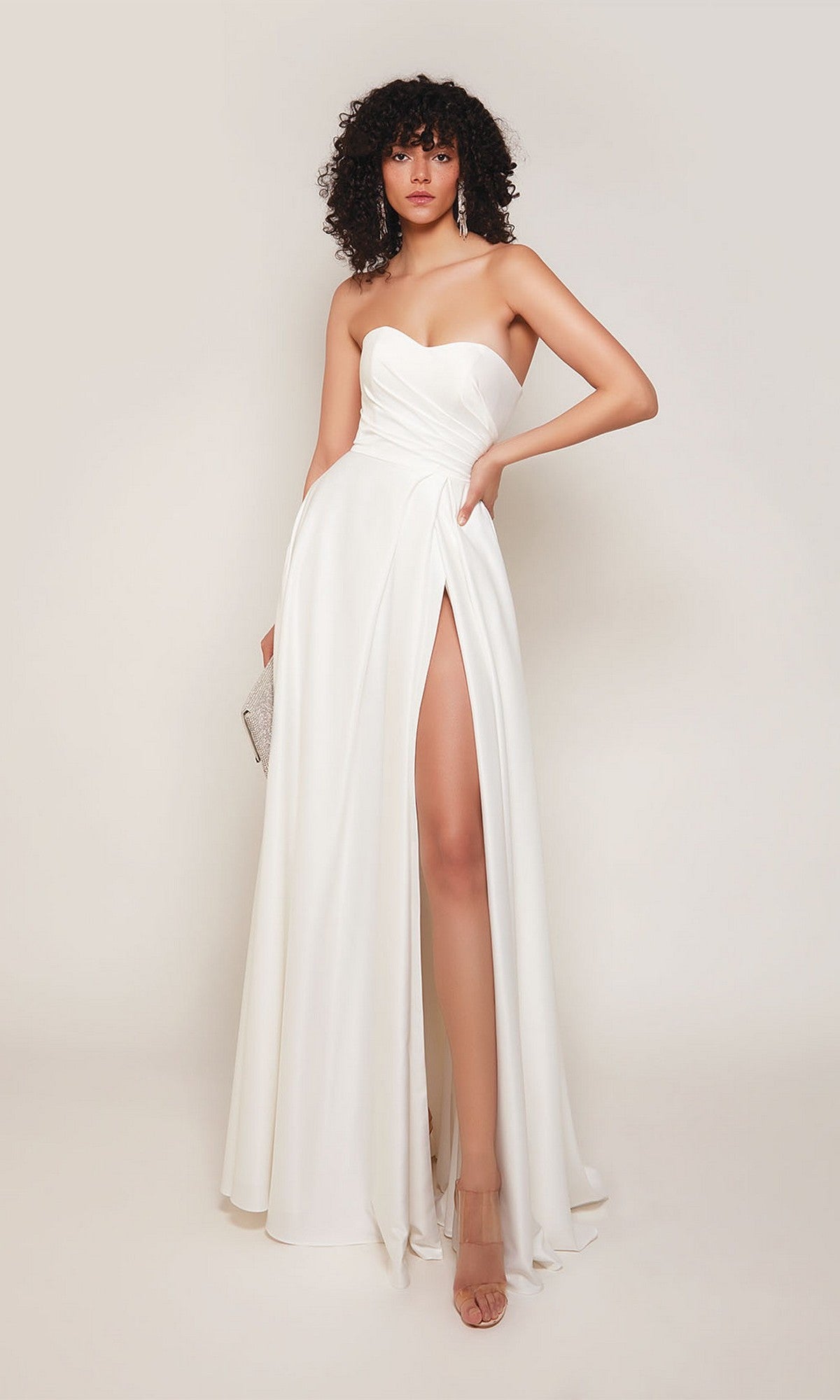 A woman in the Alyce 7088 long formal dress in diamond white, featuring a strapless design and high slit, holds a small clutch against a plain background.