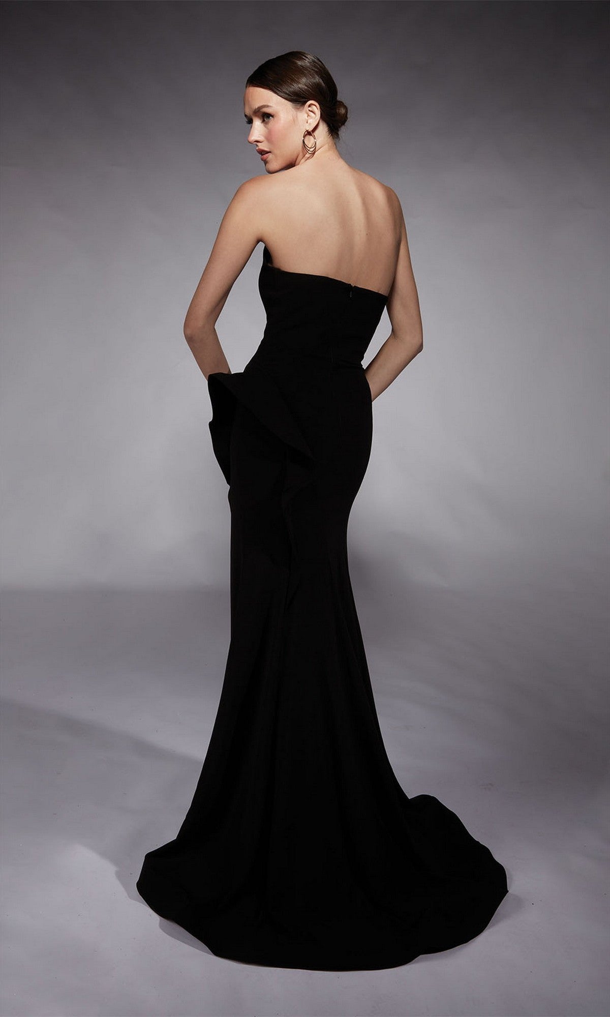 A woman models the Alyce 7113 long formal dress—a fitted, strapless black gown with a flared hem—posing against a plain studio background, ideal for special occasions.