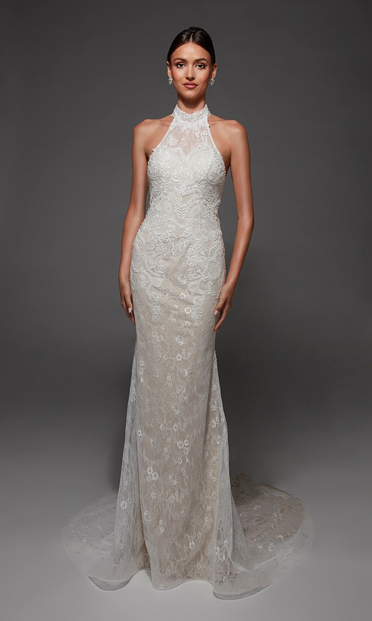 A woman wears the Long Wedding Dress: Alyce 7173 in Diamond White/Light Latte—a sleeveless, high-neck lace gown with a fitted bodice, elegant open back, and a slight train—standing against a dark gray background.