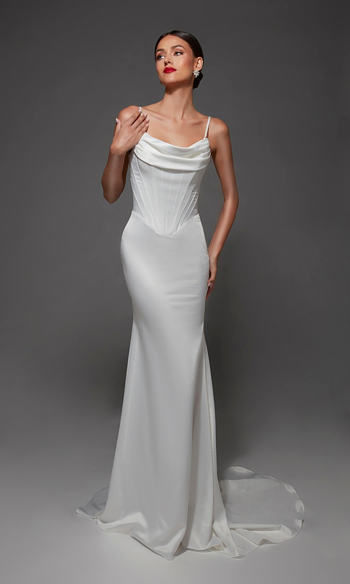 A woman models the Long Wedding Dress: Alyce 7175, a white fitted satin gown featuring a corset bodice, spaghetti straps, cowl neckline, and a floor-length skirt with a small train.