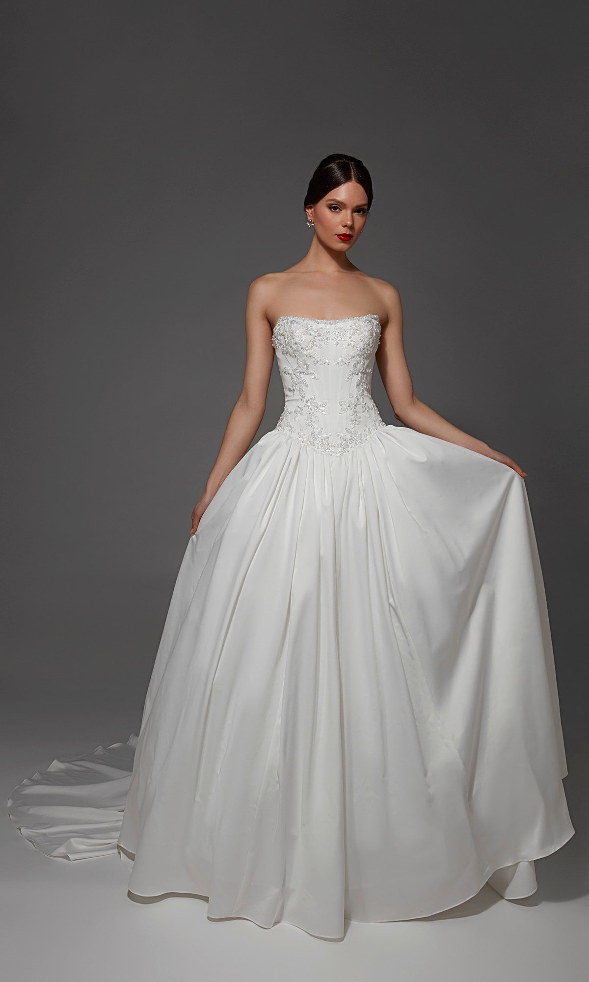 A woman models the Alyce 7188 long wedding dress, a strapless satin ball gown featuring floral embroidery and a subtle sweetheart neckline, set against a plain dark backdrop.