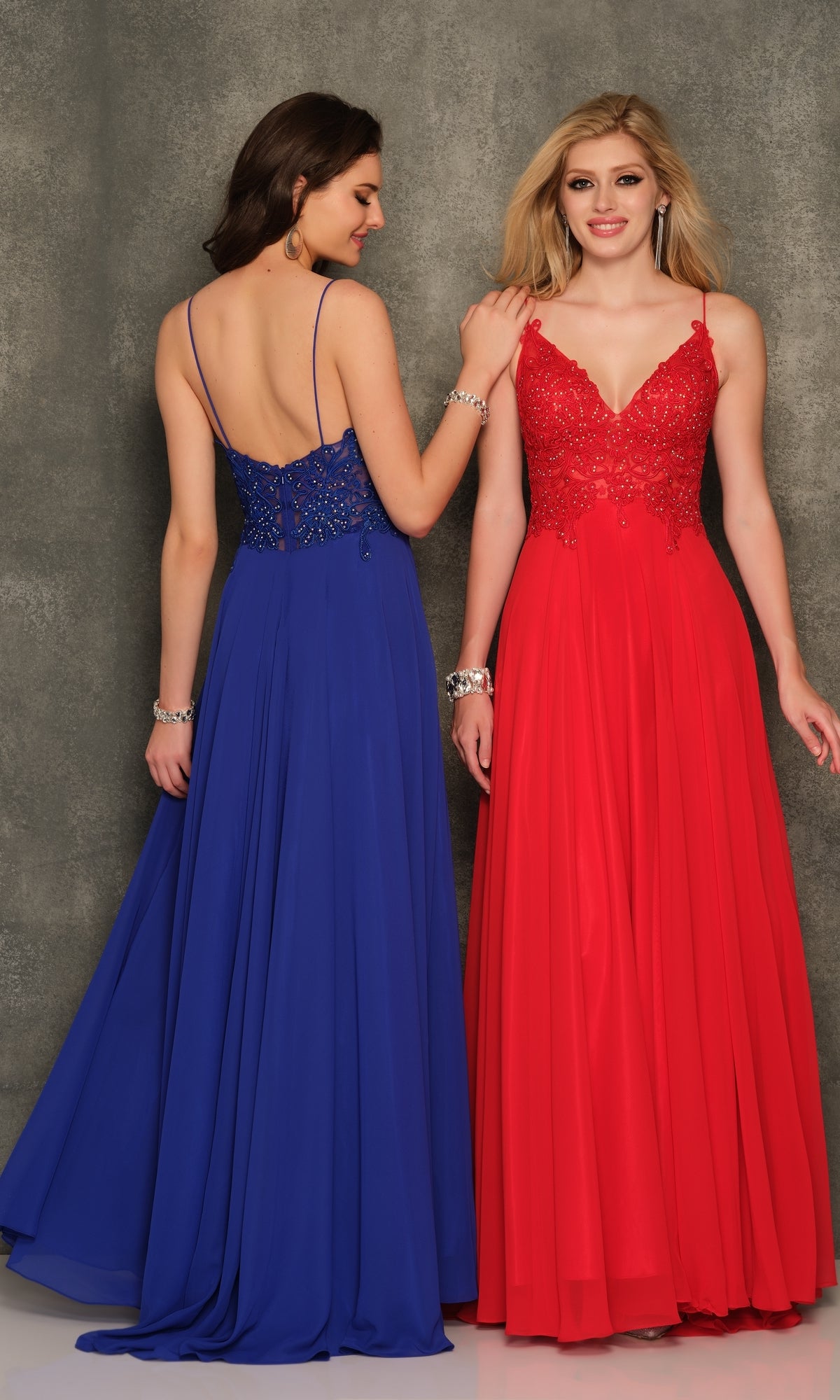 Two women wear Classic Long A-Line Prom Gown: Dave & Johnny A7248 in red and blue, featuring embroidered-lace bodices and spaghetti straps, standing against a textured gray background.