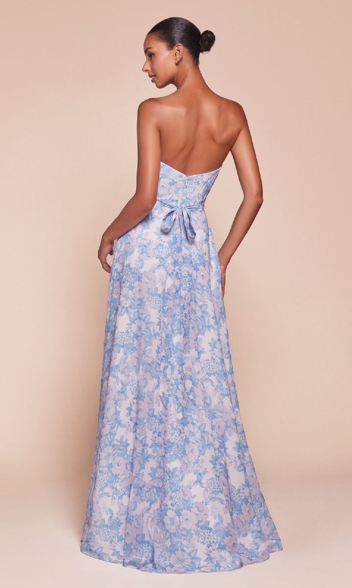 A woman models the Strapless Long Print Prom Dress CL7443, featuring a floor-length blue and pink floral print, sweetheart neckline, and a bow at the fitted back, against a light beige background.