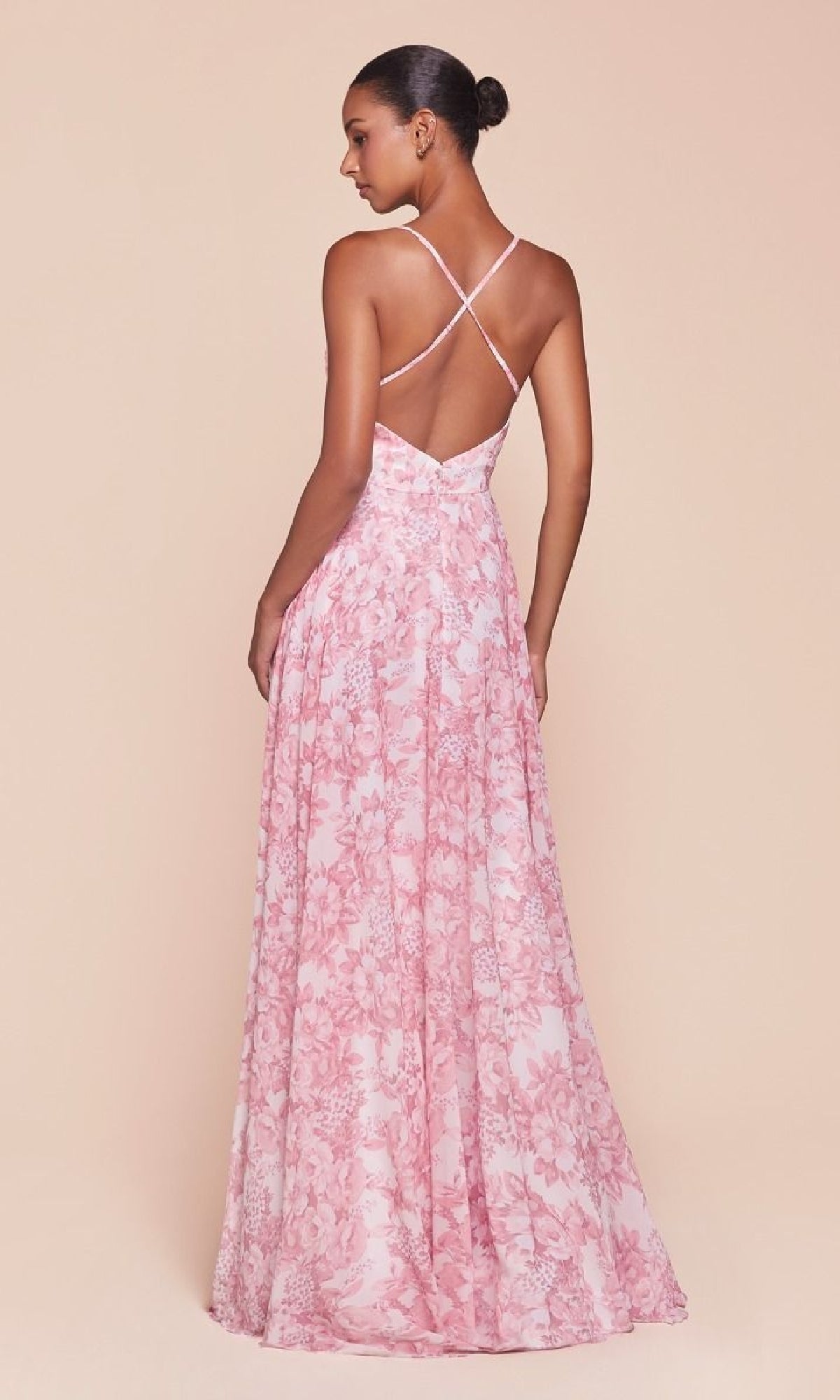 A woman stands against a beige background, facing away, in the Ladivine 7444 Floral-Print Long A-Line Prom Dress featuring a pink floral pattern, backless floor-length design, and crisscross straps.