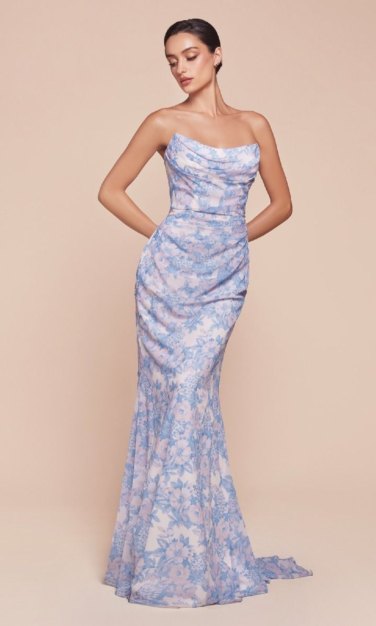 A woman models the Ladivine 7445 strapless long floral-print prom dress with blue flowers on sheer fabric, featuring a fitted bodice—an elegant evening gown for under $150, shown against a plain beige background.