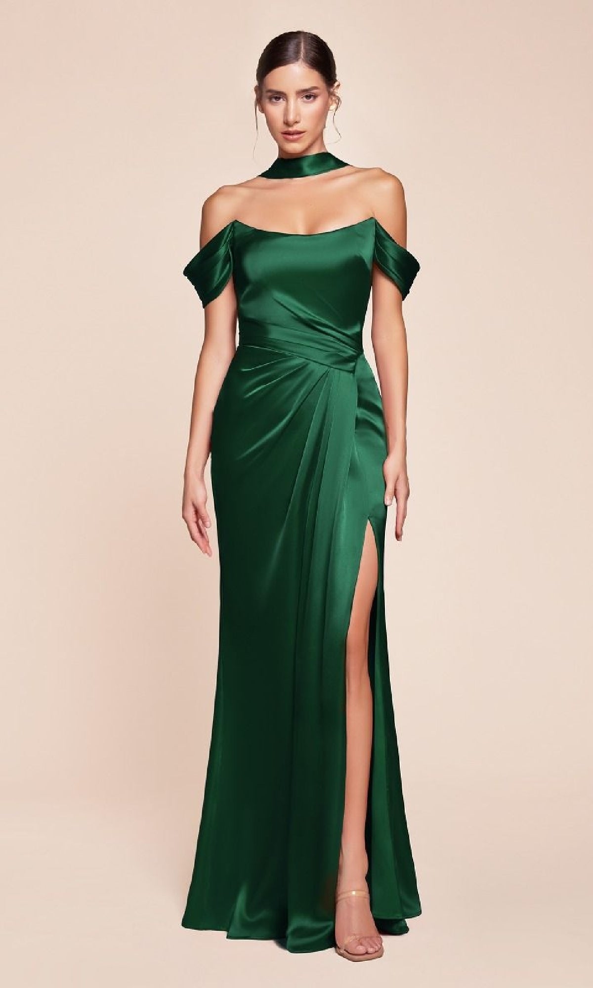 A woman stands against a plain beige background wearing the Lace-Up Off-Shoulder Prom Dress: Ladivine 7452, an emerald green satin formal gown with a thigh-high slit, matching neckband, and strappy heels.